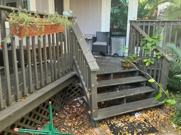 Wooden porch stairs with gray railings, potted plants, and fallen leaves in a backyard.