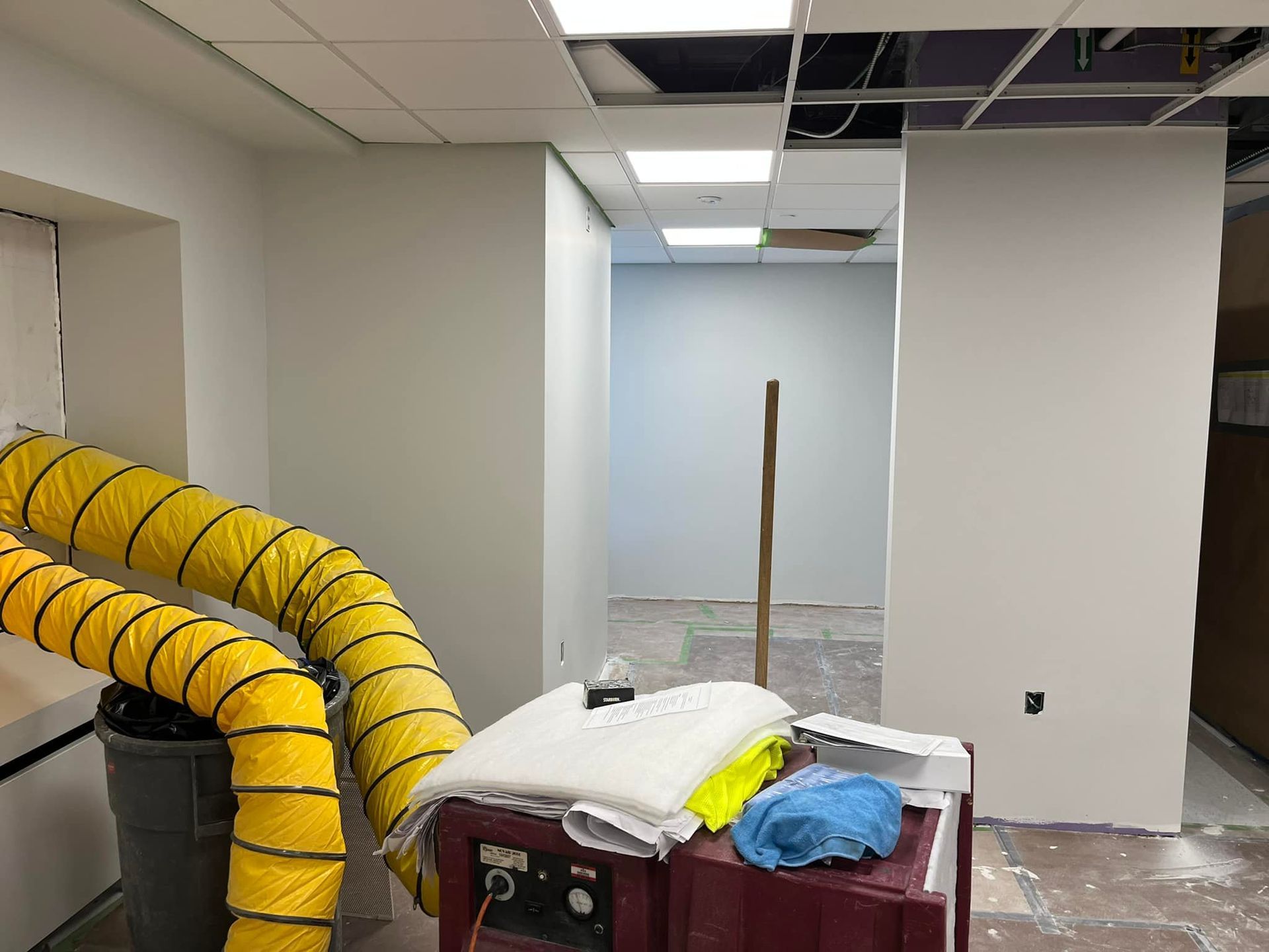 Office under renovation with exposed ceiling, yellow ventilation hose, and tools on a cart