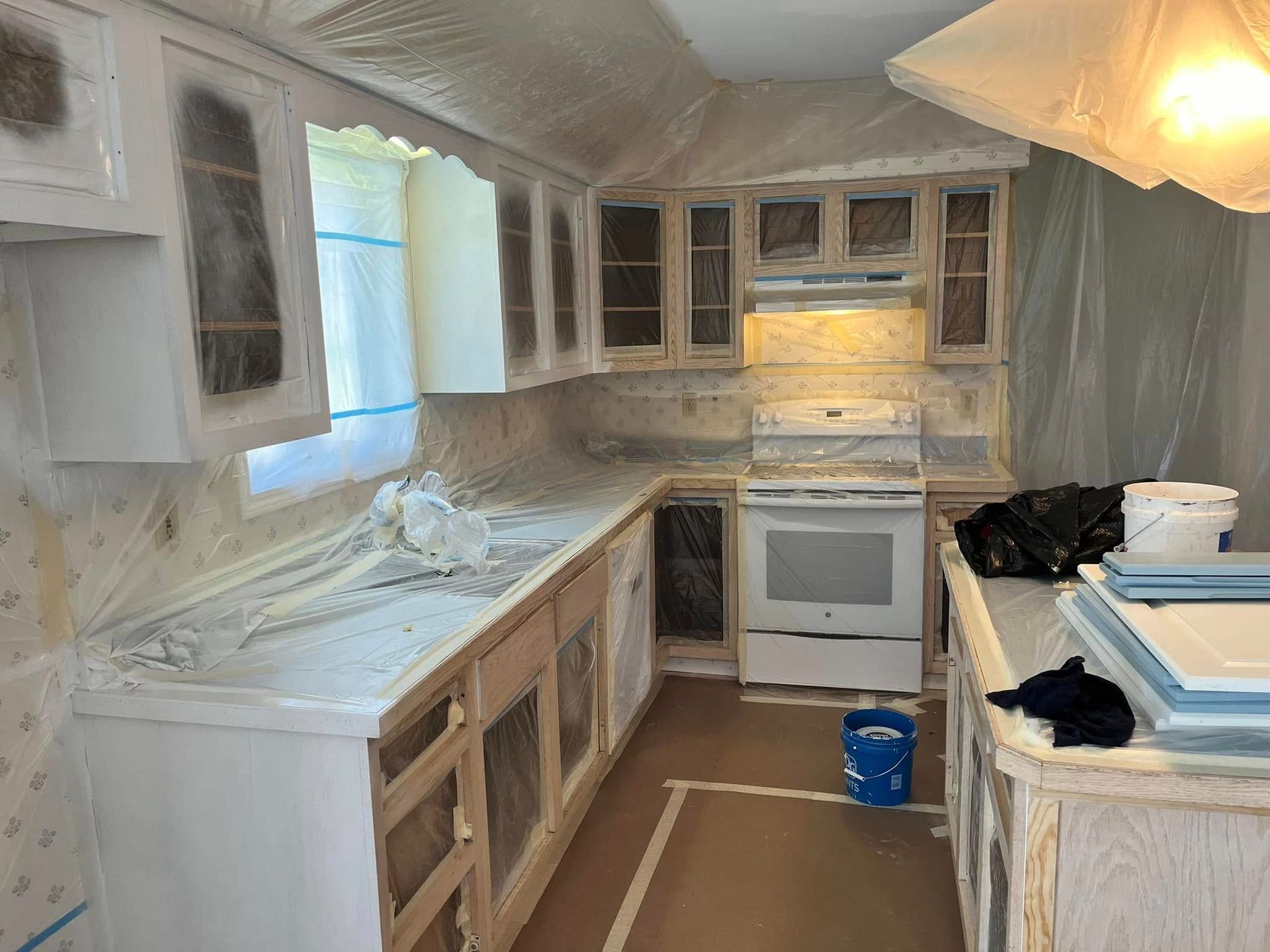Partially renovated kitchen with white cabinets, countertops covered in plastic, and an oven under construction