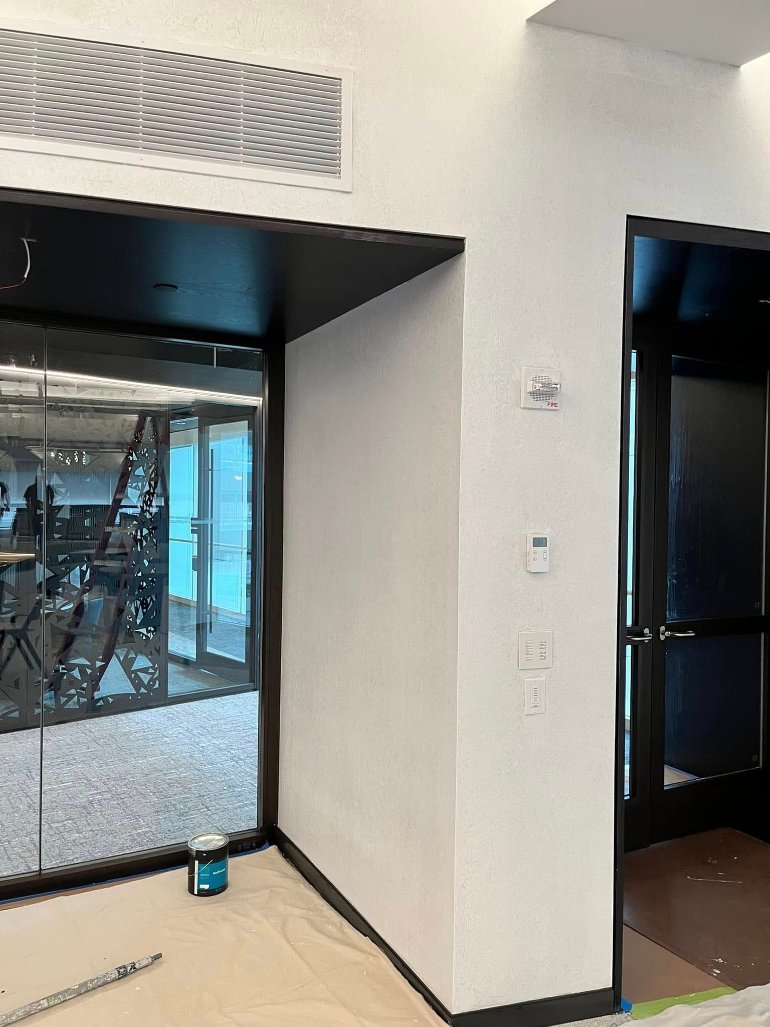 Empty storefront interior with glass storefront windows and a doorway, showing a partially finished floor and wall vent.