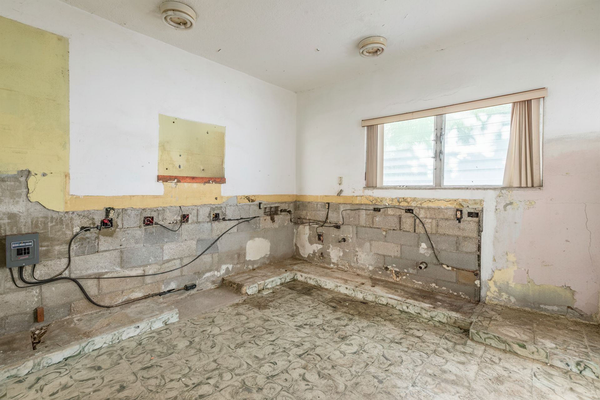 Damaged kitchen with stripped walls, exposed wiring, and debris on the floor