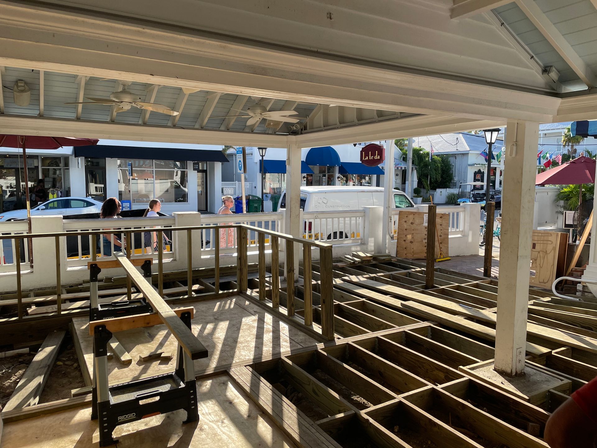 Partially demolished deck with exposed wooden joists under a covered patio, overlooking a street
