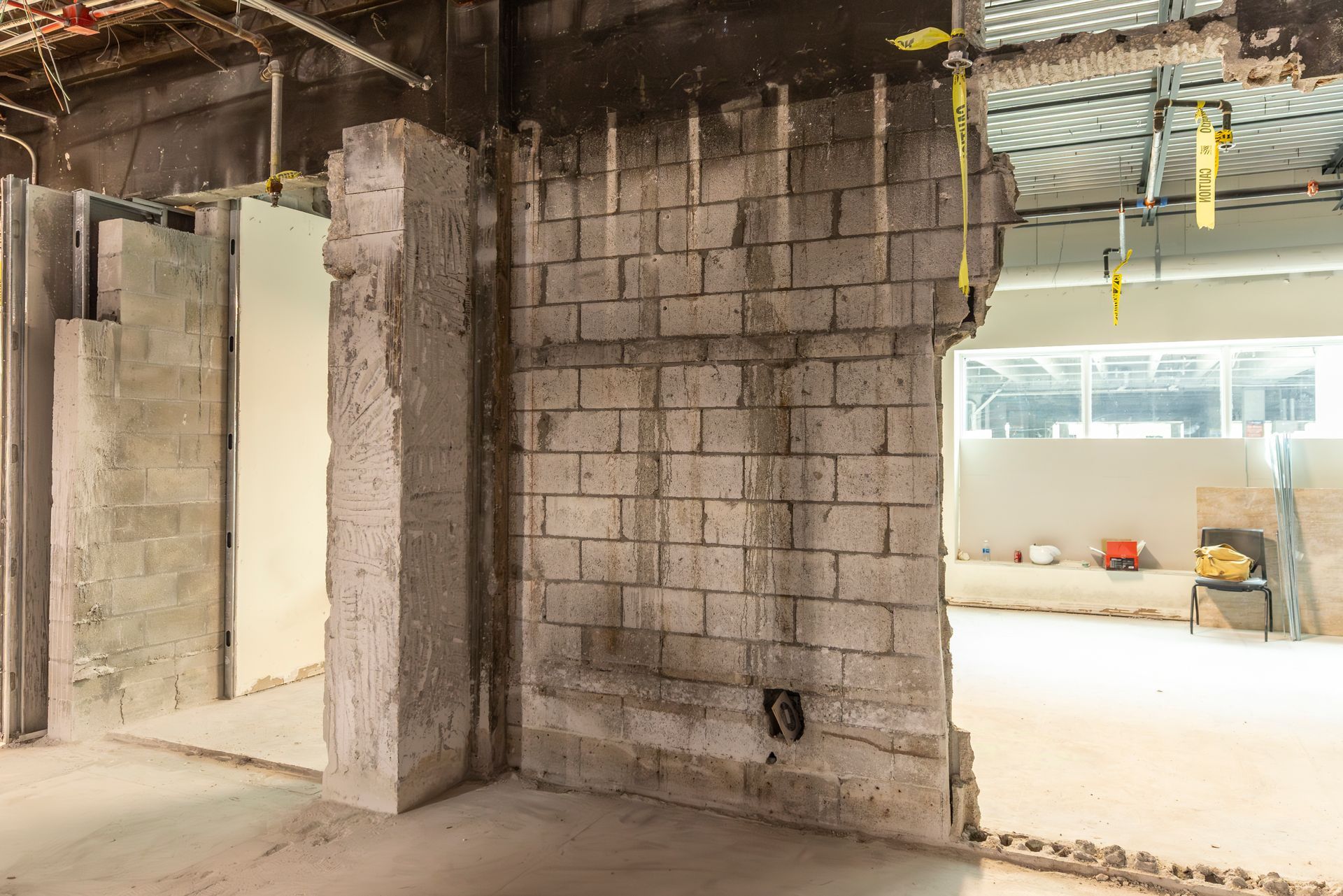 Unfinished construction interior with cinderblock walls, concrete column, and open doorway to a lit room