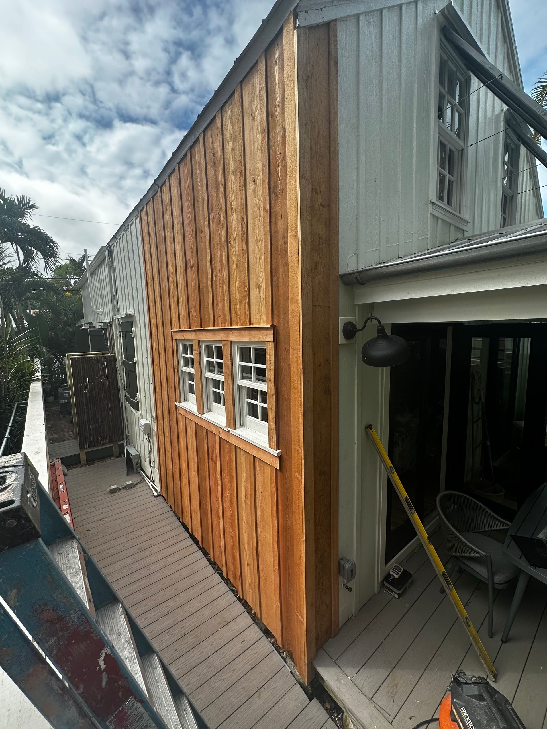 Wood-sided building exterior with white-framed windows beside a covered walkway and open garage-like area