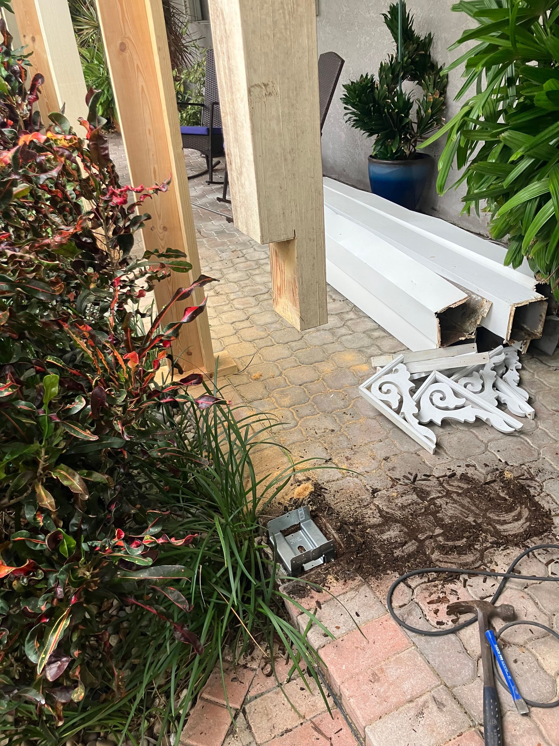 Outdoor walkway with stacked white pipes, tools, and garden plants beside a patio column.