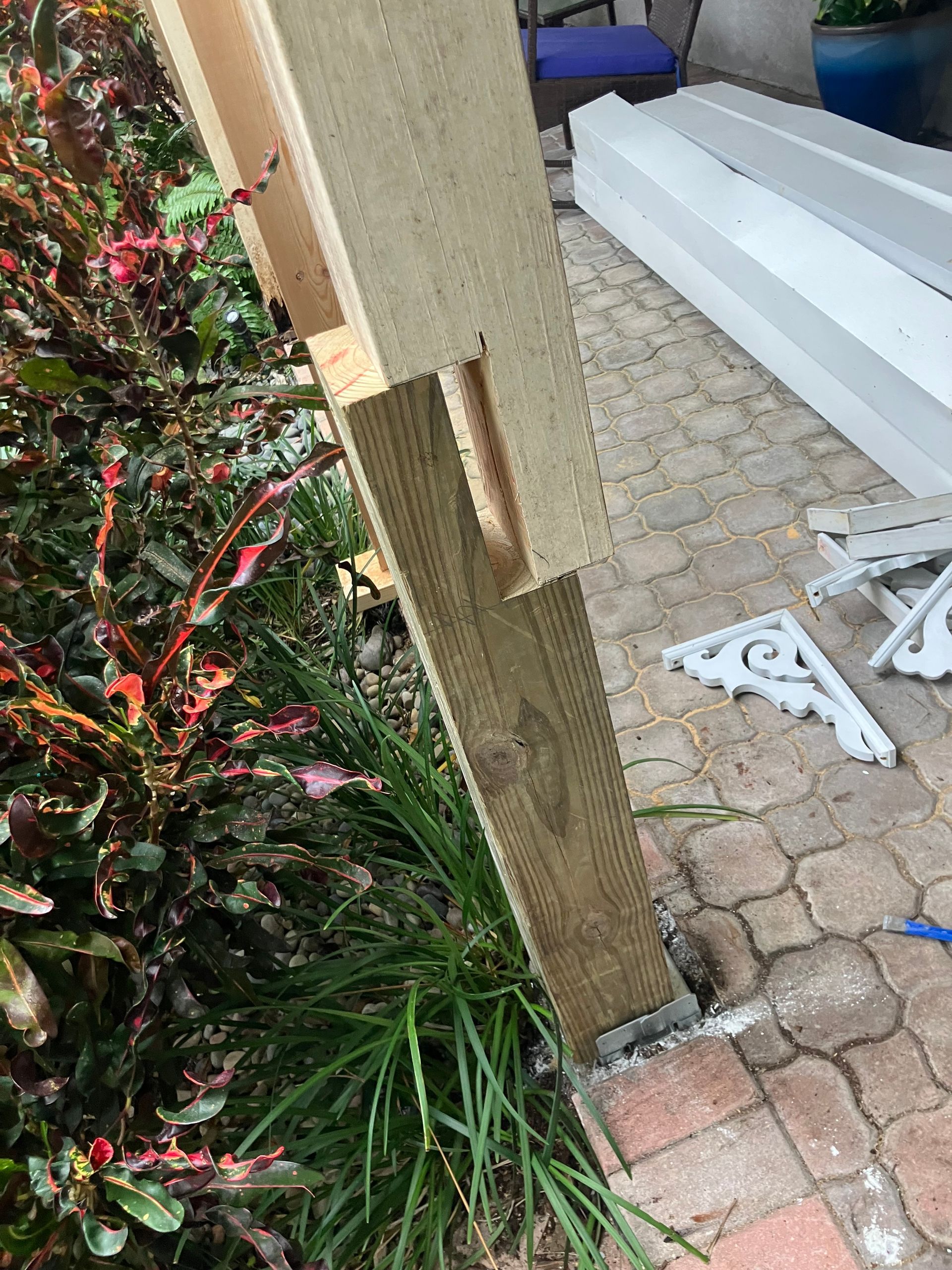 Wooden fence post beside a garden bed and brick walkway, with steps and a white metal bracket nearby.