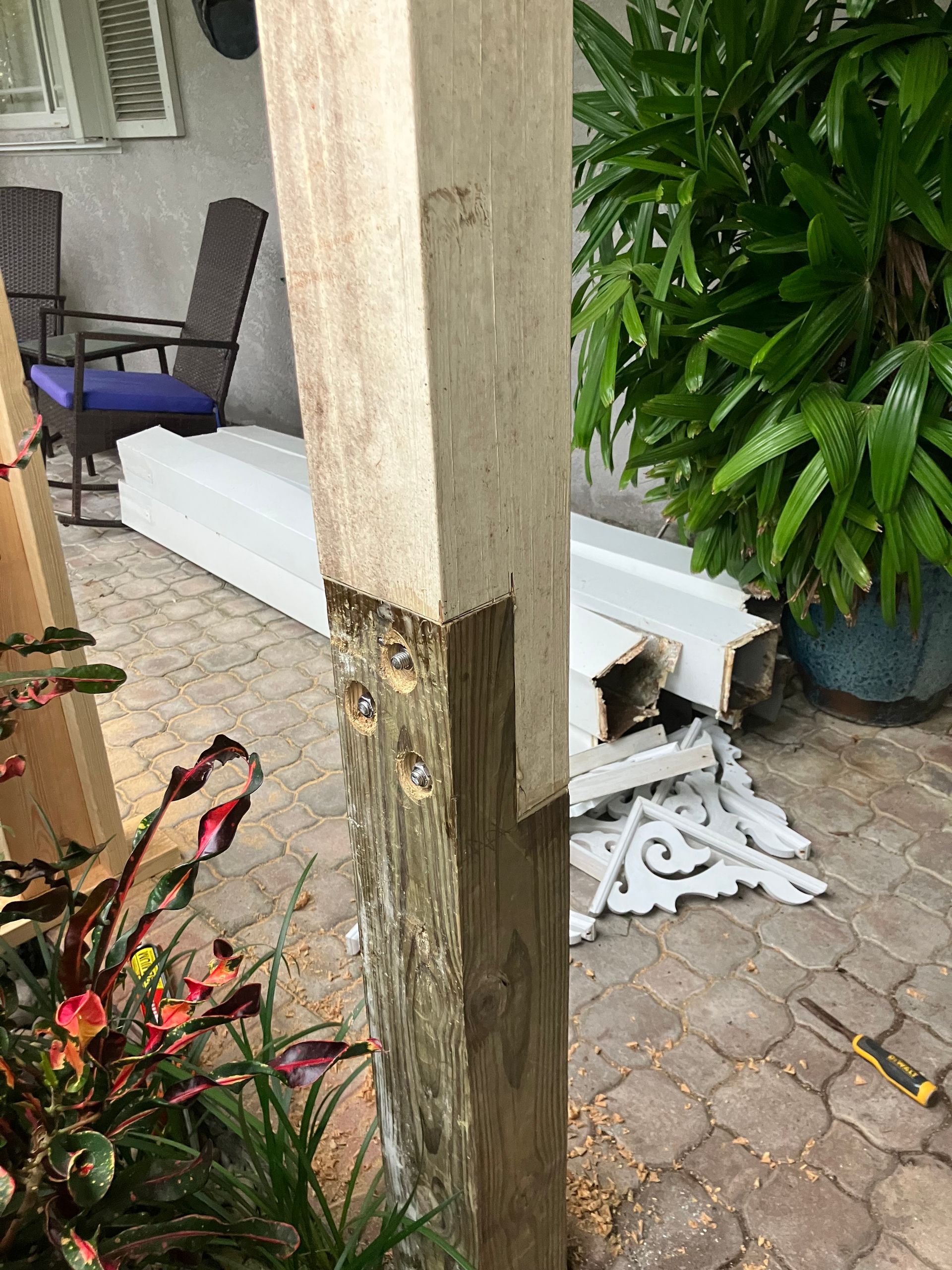 Damaged porch post with rotted wood near a white bench and potted plants on a patio