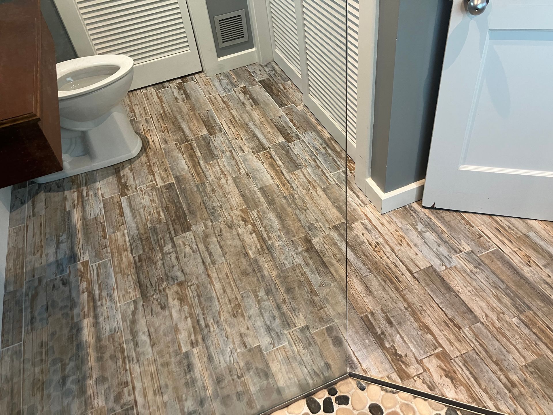 Small bathroom with wood-look flooring, toilet, and open louvered closet doors.