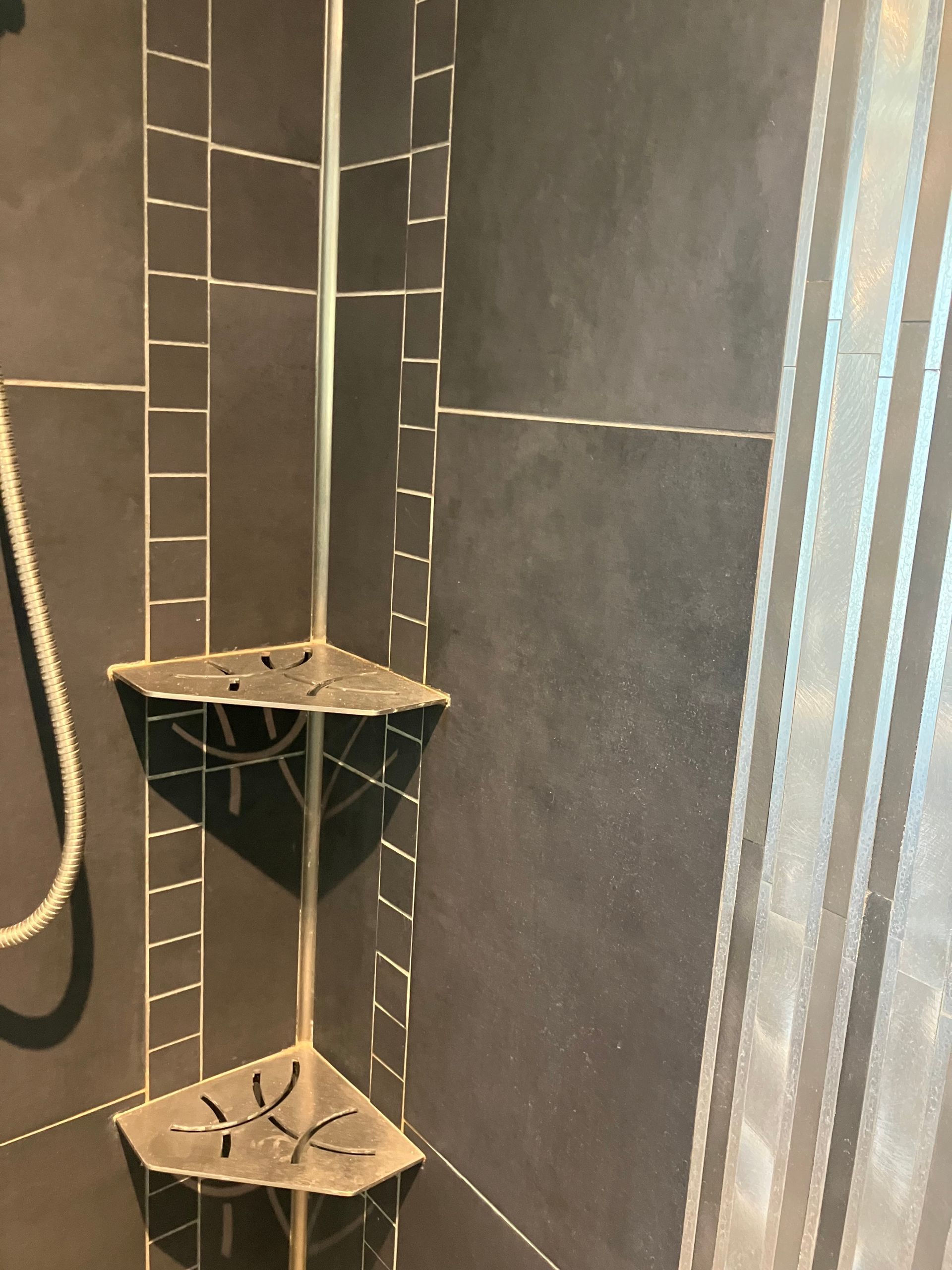 Black-tiled shower corner with two triangular corner shelves and a hanging rope shower handle