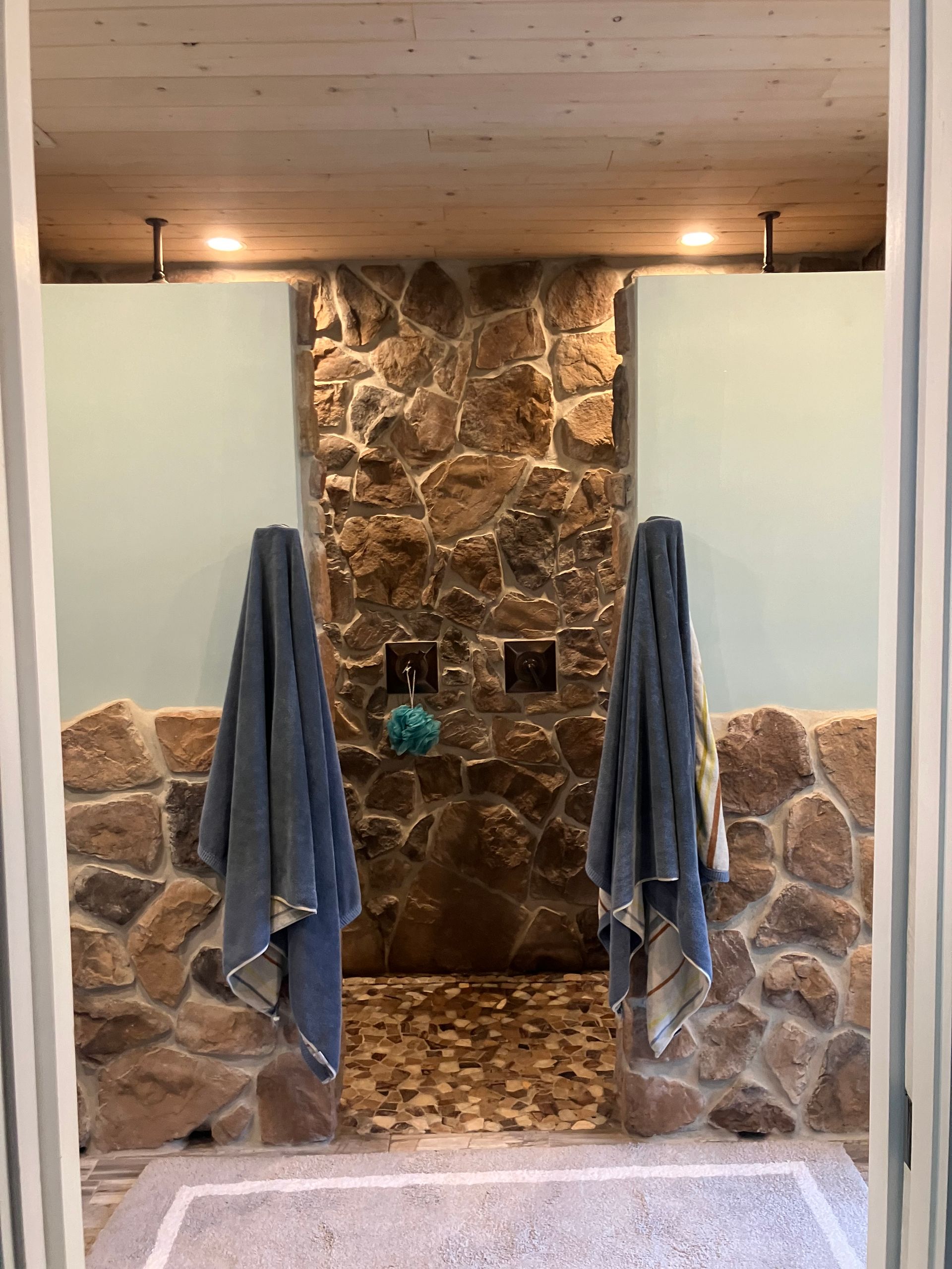 Stone shower alcove with two blue towels hanging on hooks and a wood ceiling.