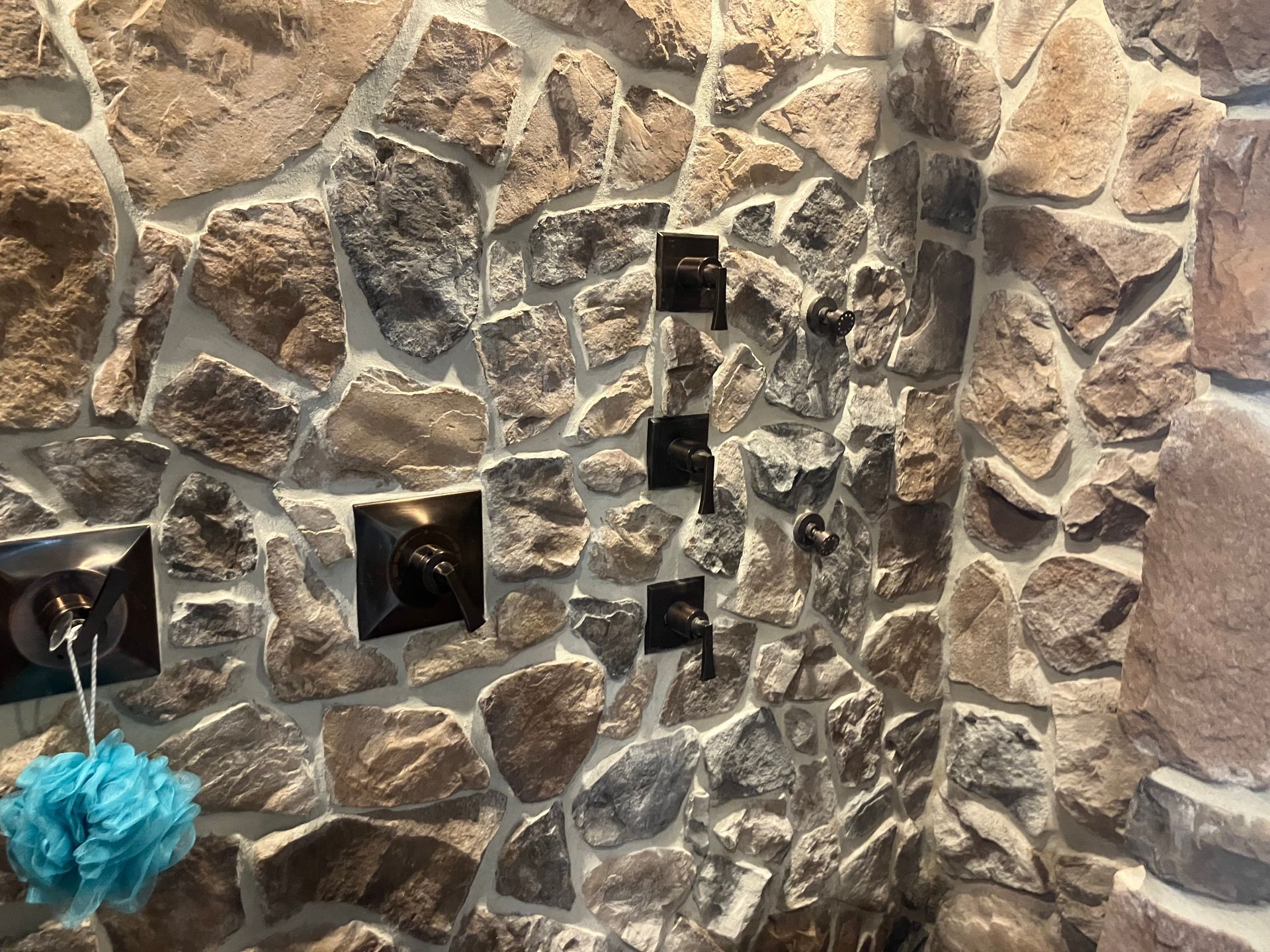 Stone wall with dark electrical outlets and a blue bath pouf hanging at the lower left.