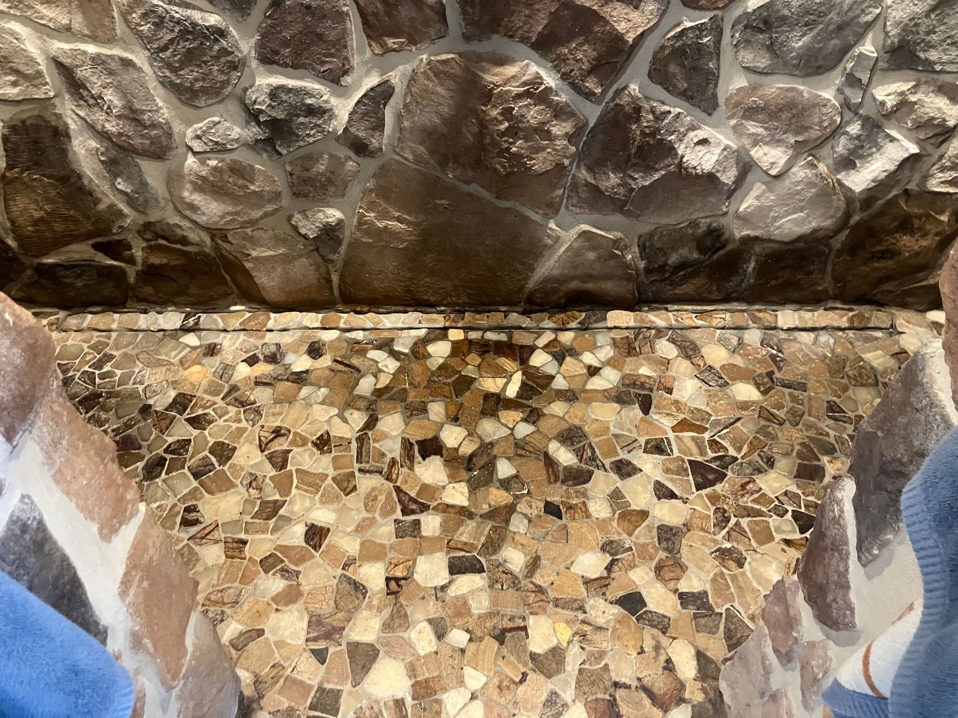 Mosaic-tiled shower floor meeting a stone wall, with blue and white tiled sides.