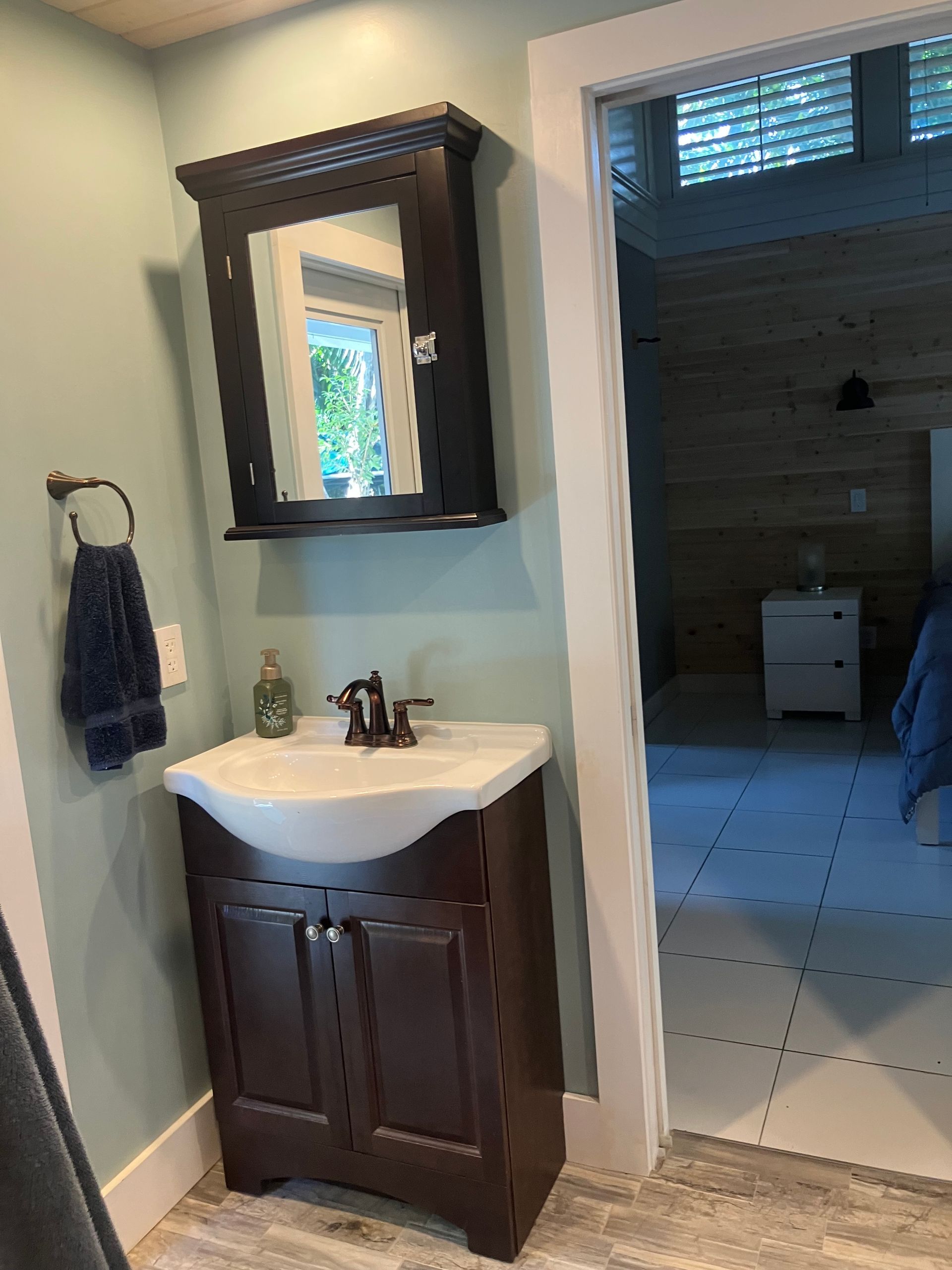 Bathroom vanity with dark wood cabinet, white sink, mirror cabinet, and doorway to tiled room beyond