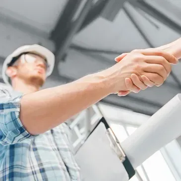 Worker in a hard hat shaking hands indoors near a staircase and metal beams