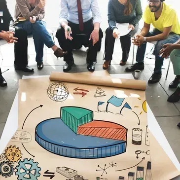People gathered around a floor chart with colorful 3D bar graphs and business sketches.