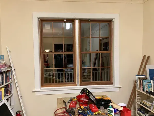 Window in a beige room with ladders and cleaning supplies stacked below it