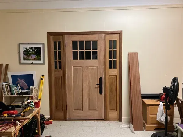 Wooden double front door in a cluttered room with shelves, tools, and a fan on the right.