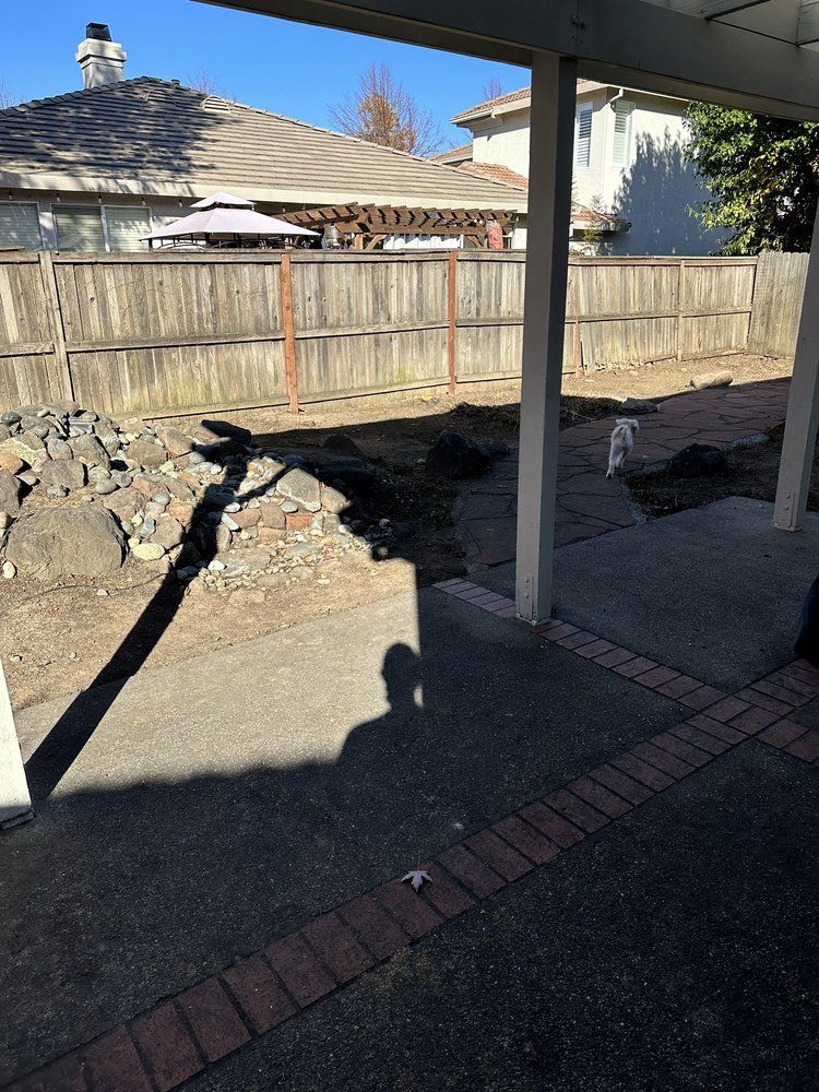 A shadow of a person is cast on the sidewalk in front of a wooden fence.