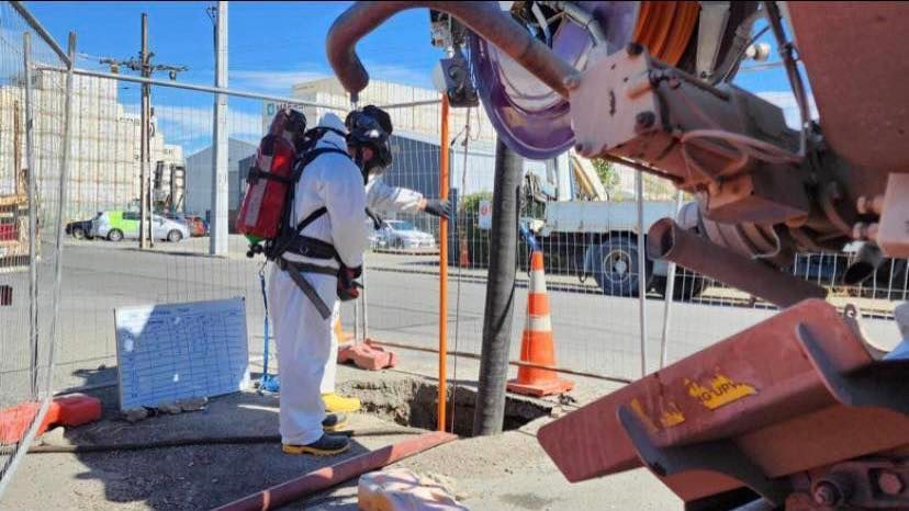 A man in a protective suit is standing next to a hole in the ground.