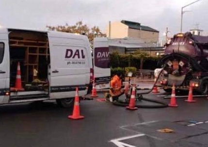 A white van with the word dal on it is parked next to a vacuum truck.