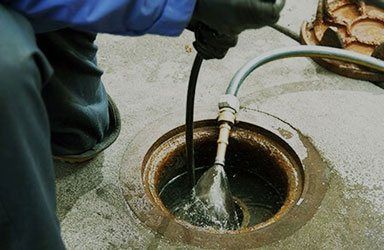 A person is cleaning a drain with a hose.