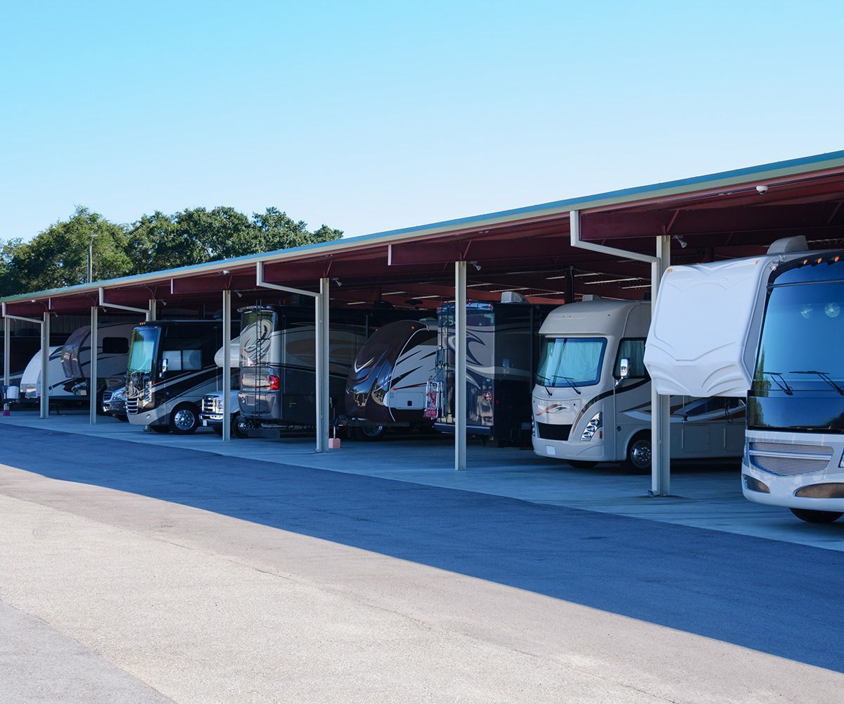 Covered parking lot with several parked RVs and vans under a long red roof on a sunny day