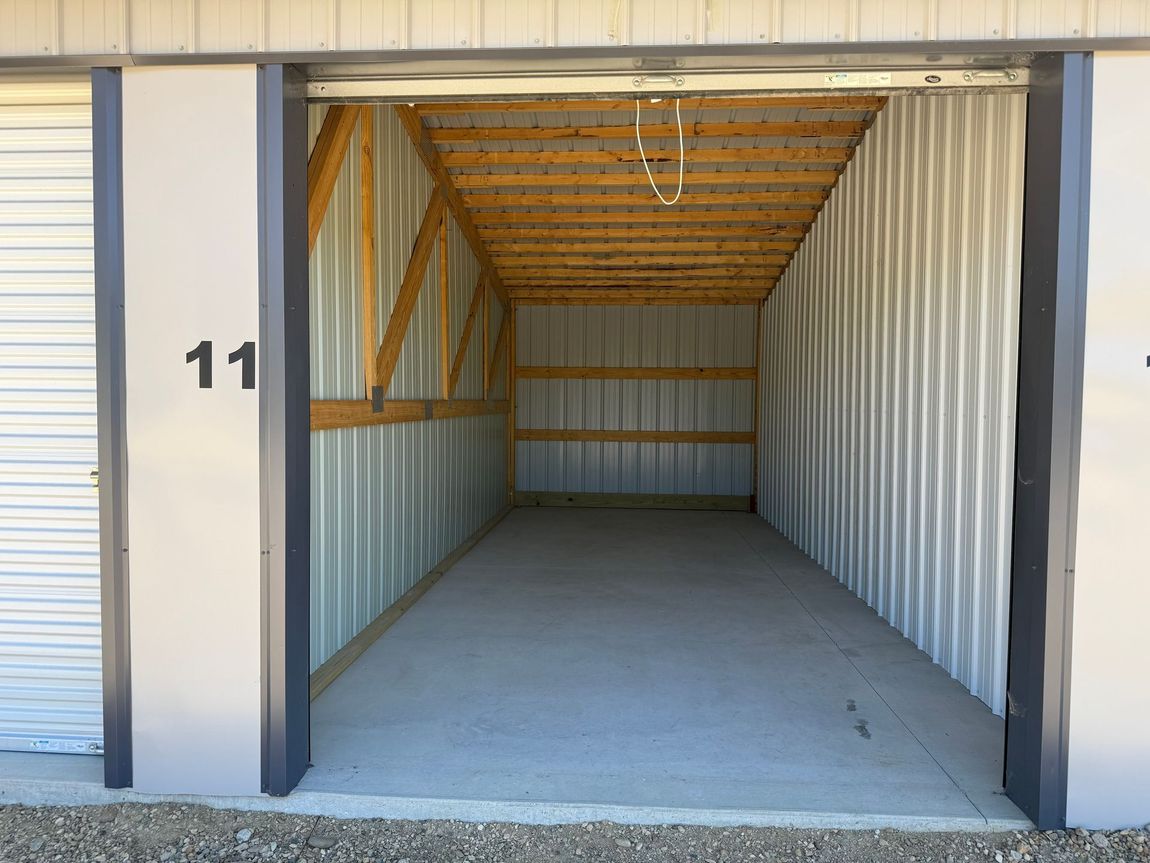 Open storage unit with white walls, wooden ceiling beams, and unit number 11.