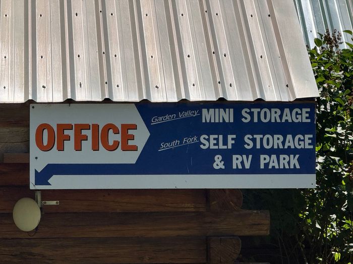 Office sign for mini storage, self storage, and RV park on a blue building.