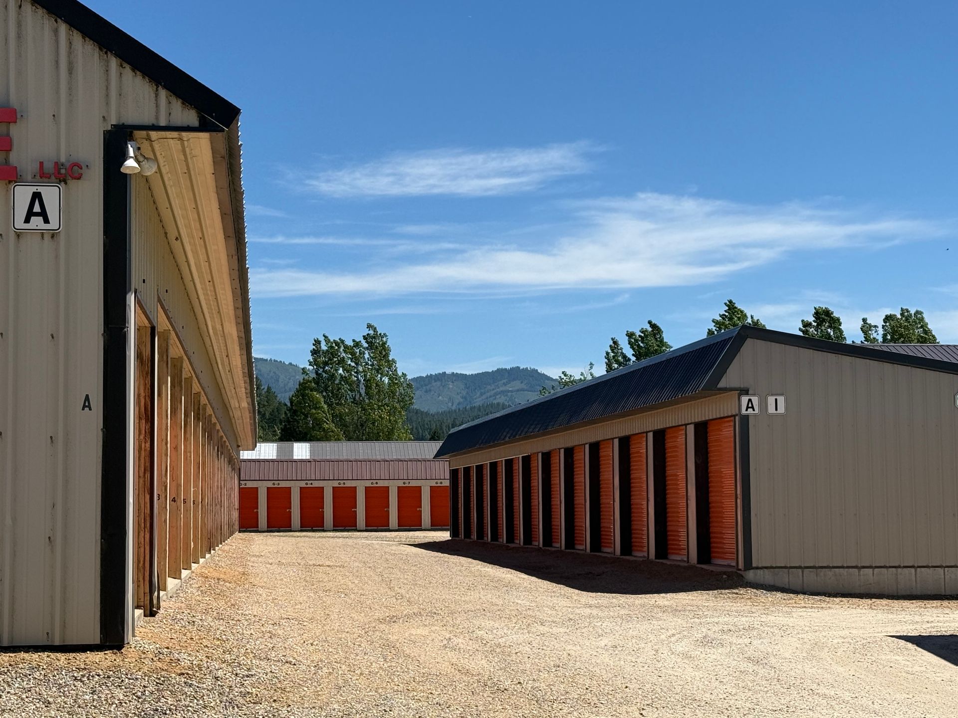 Storage units in a gravel lot, with mountains and blue sky in the background