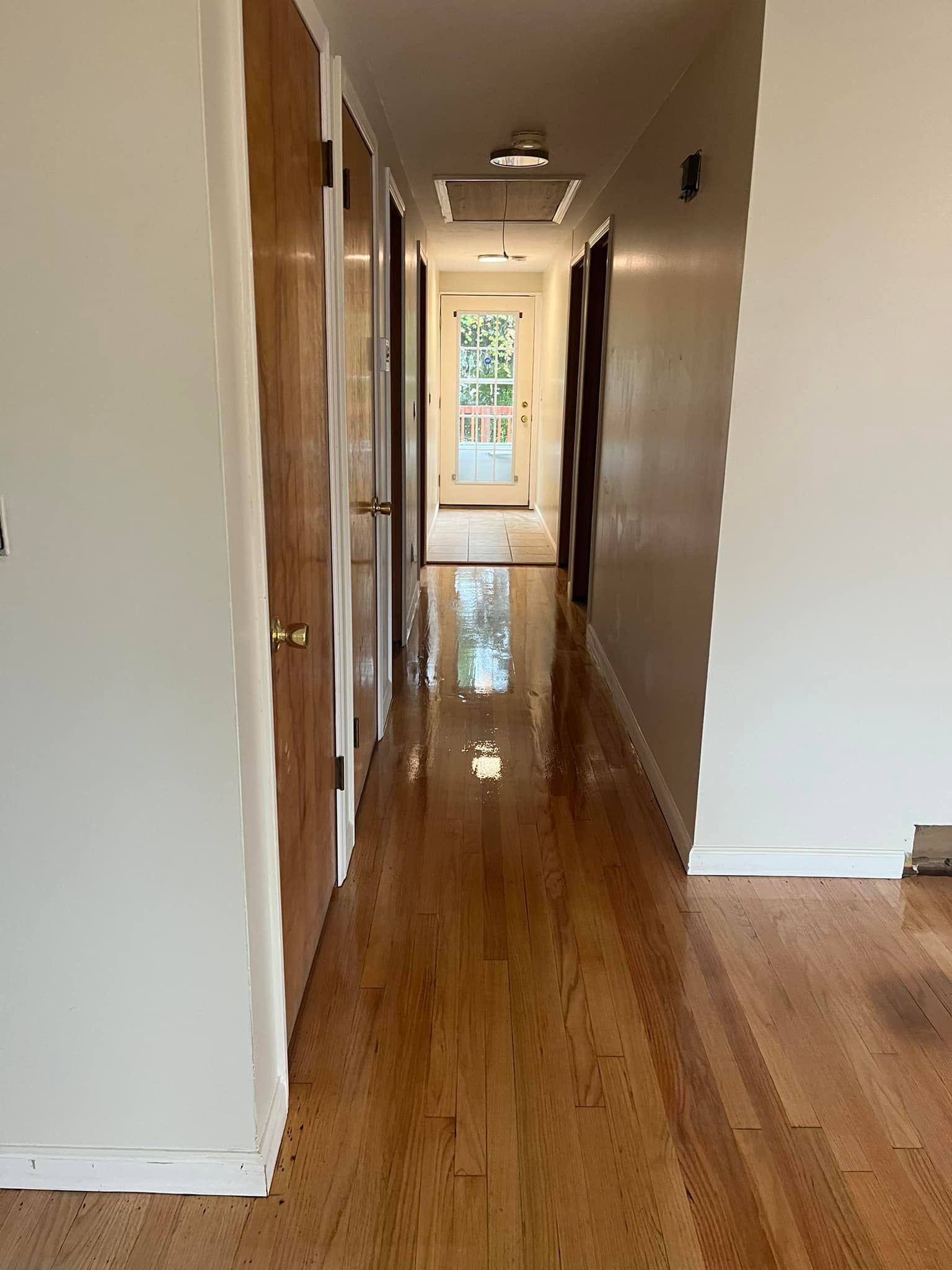 A long hallway with hardwood floors and white walls in a house.