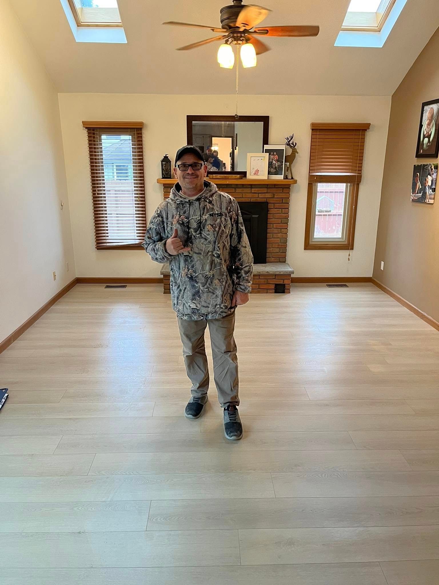 A man is standing in an empty living room with a ceiling fan.