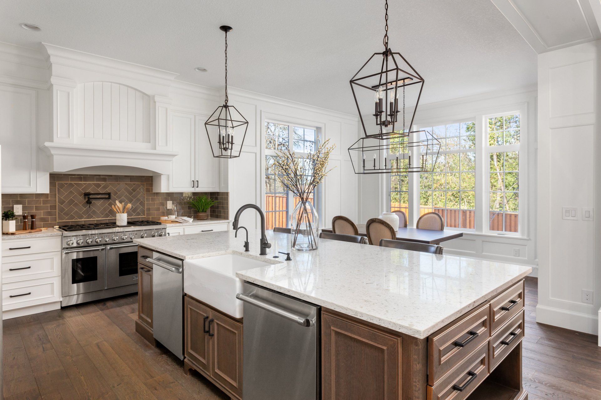 Bright modern kitchen with white island, pendant lights, stainless appliances, and large windows.