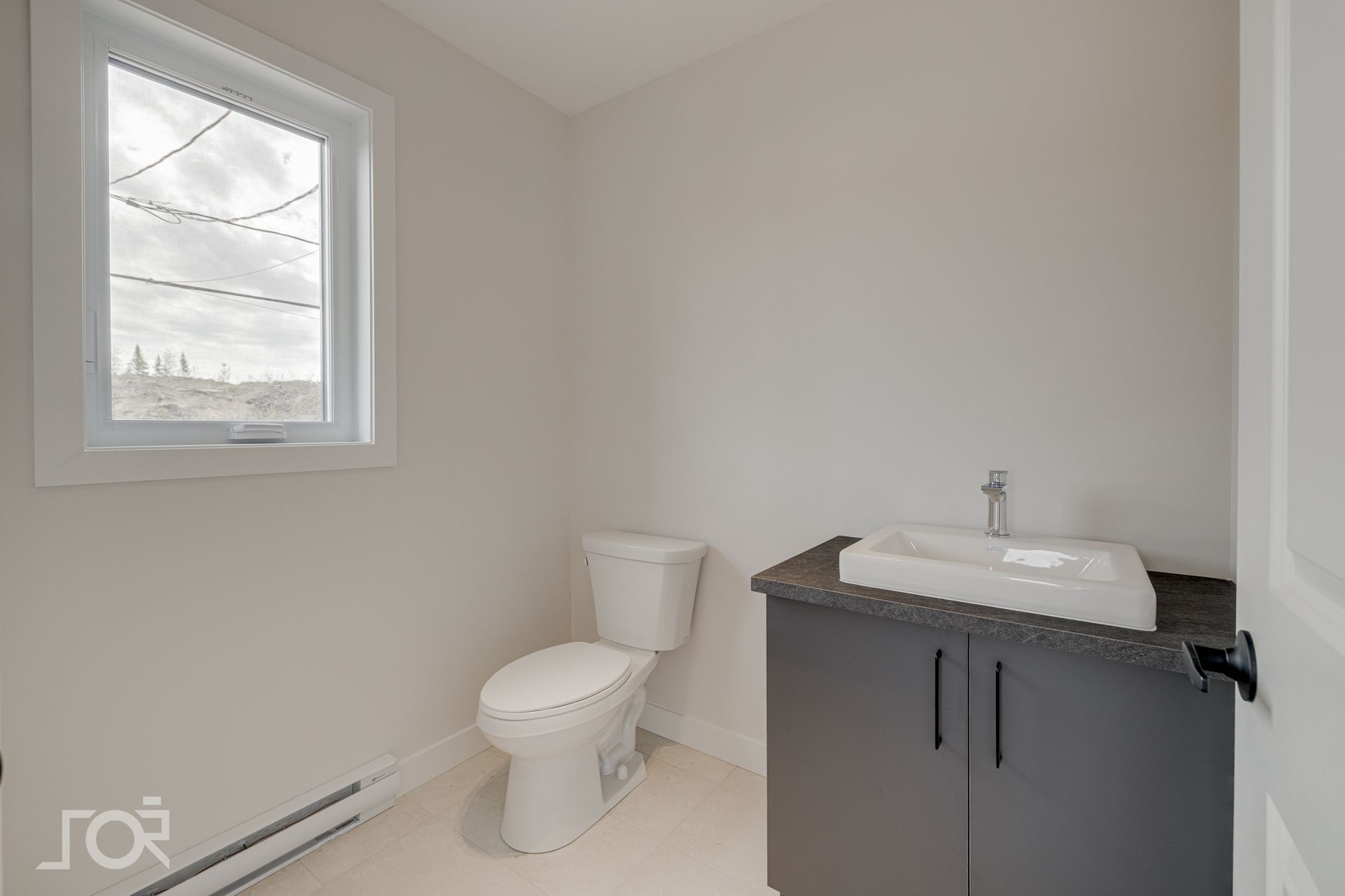 Petite salle de bains avec toilettes, meuble-lavabo, fenêtre et armoire grise.