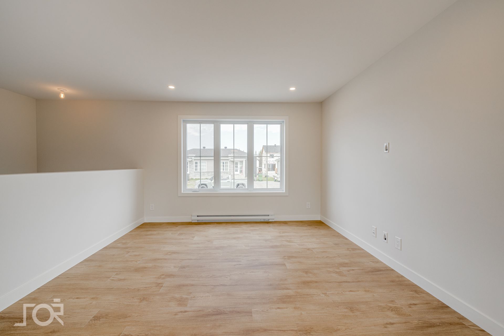 Pièce vide avec une grande fenêtre, un parquet et des murs blancs.