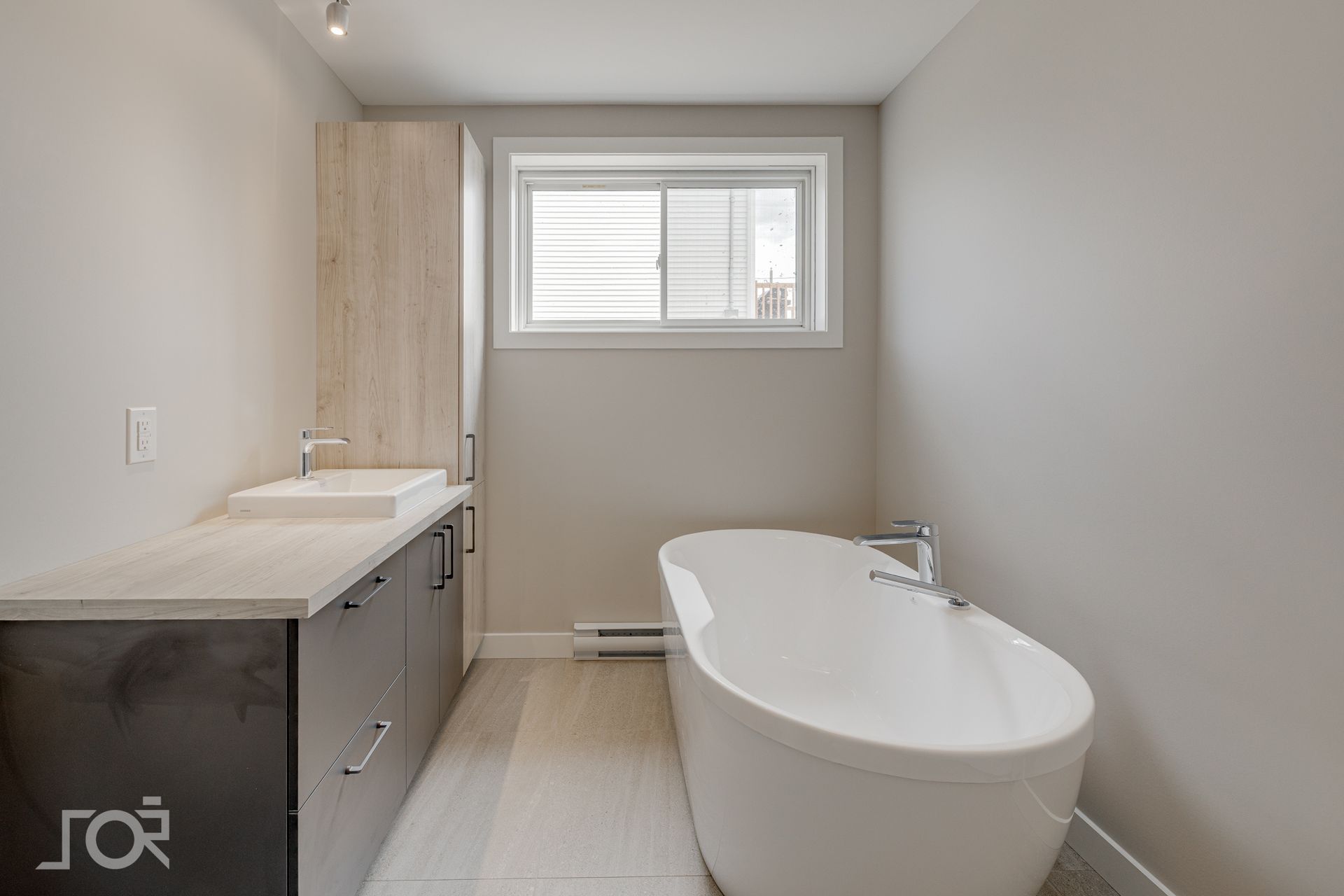 Salle de bains moderne avec baignoire blanche, meuble en bois clair et fenêtre.