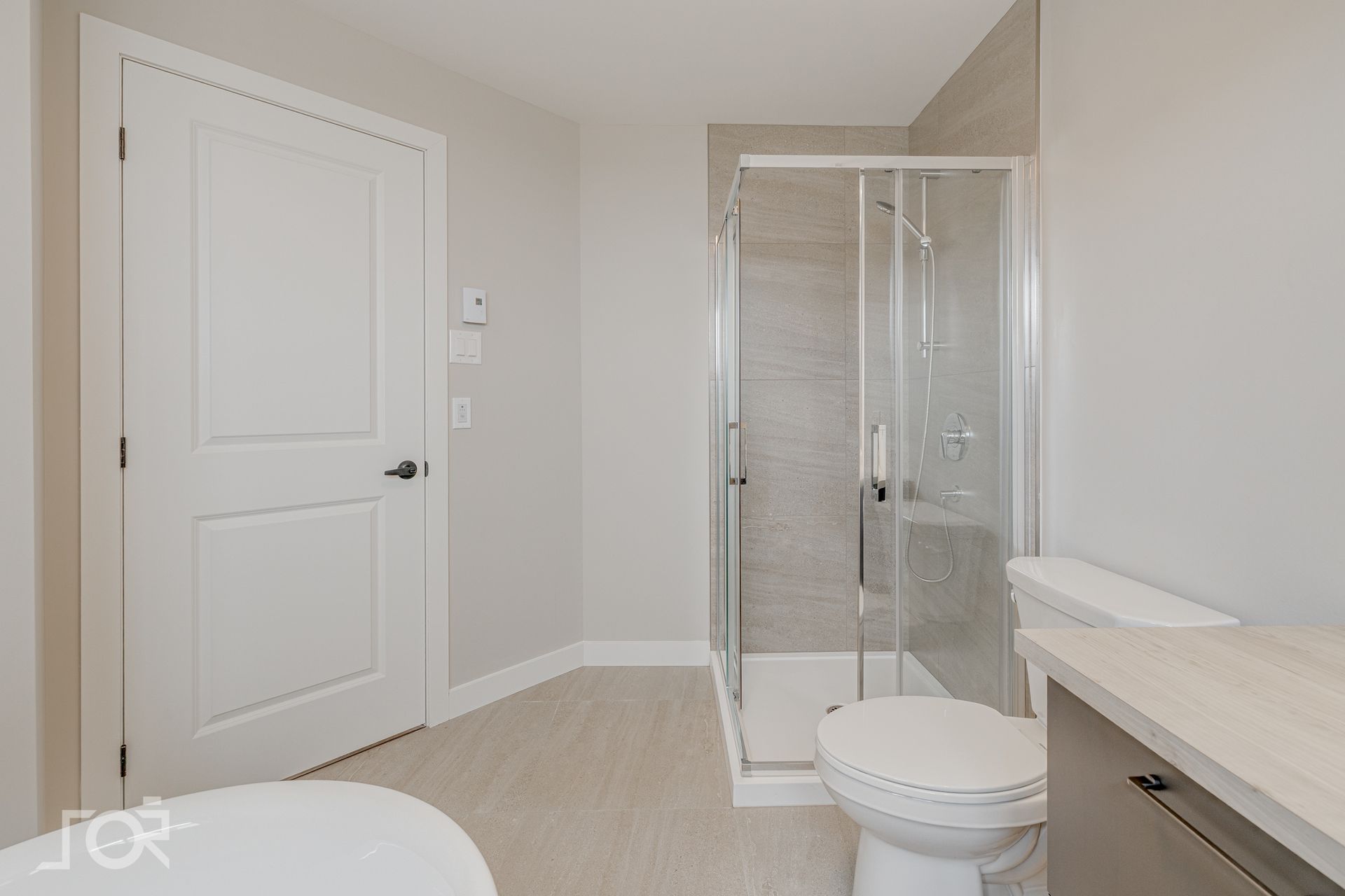 Salle de bains avec porte blanche fermée, douche en verre, toilettes et sol clair.