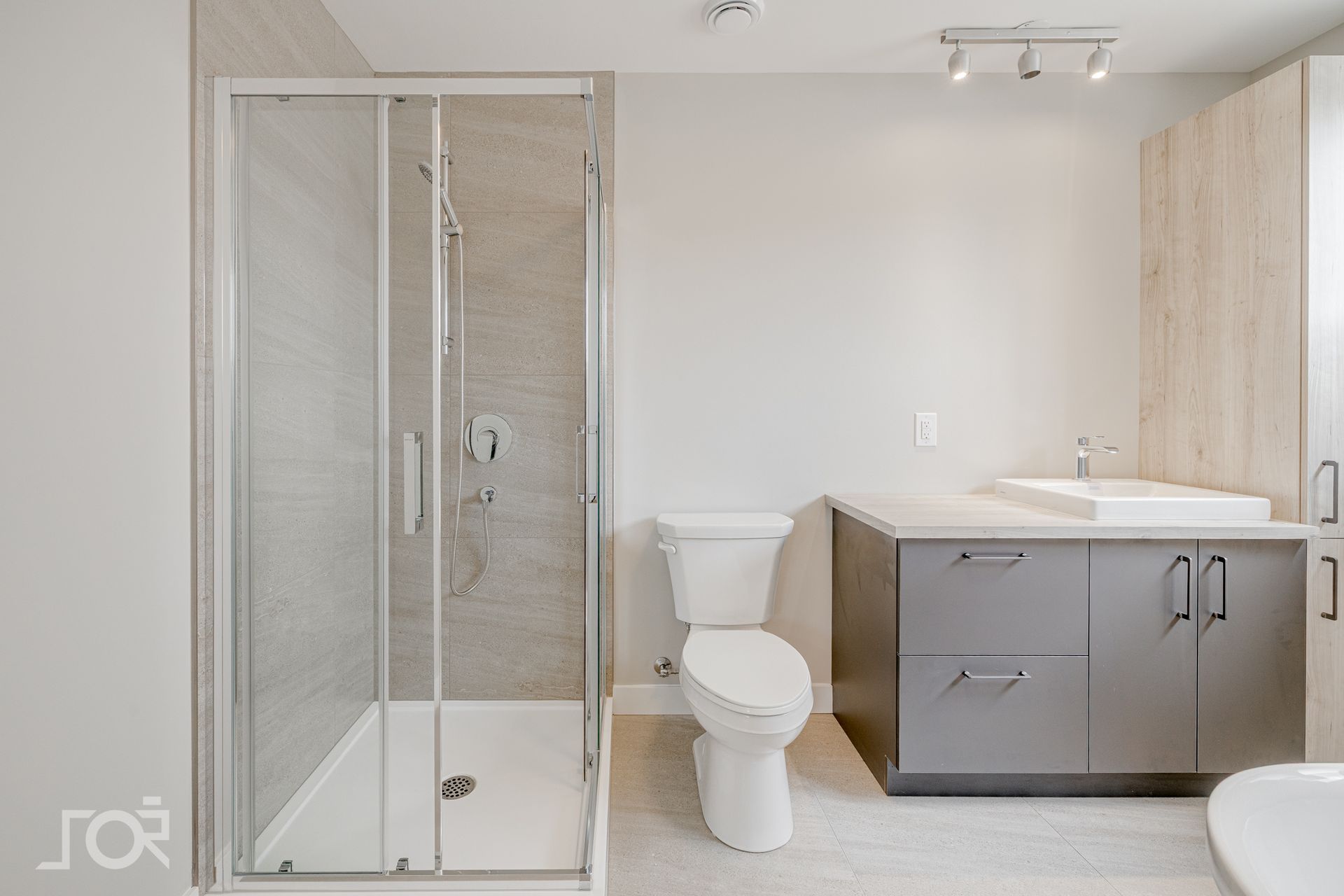 Salle de bains avec douche, toilettes et meuble-lavabo. Dominée par les tons gris et blancs.