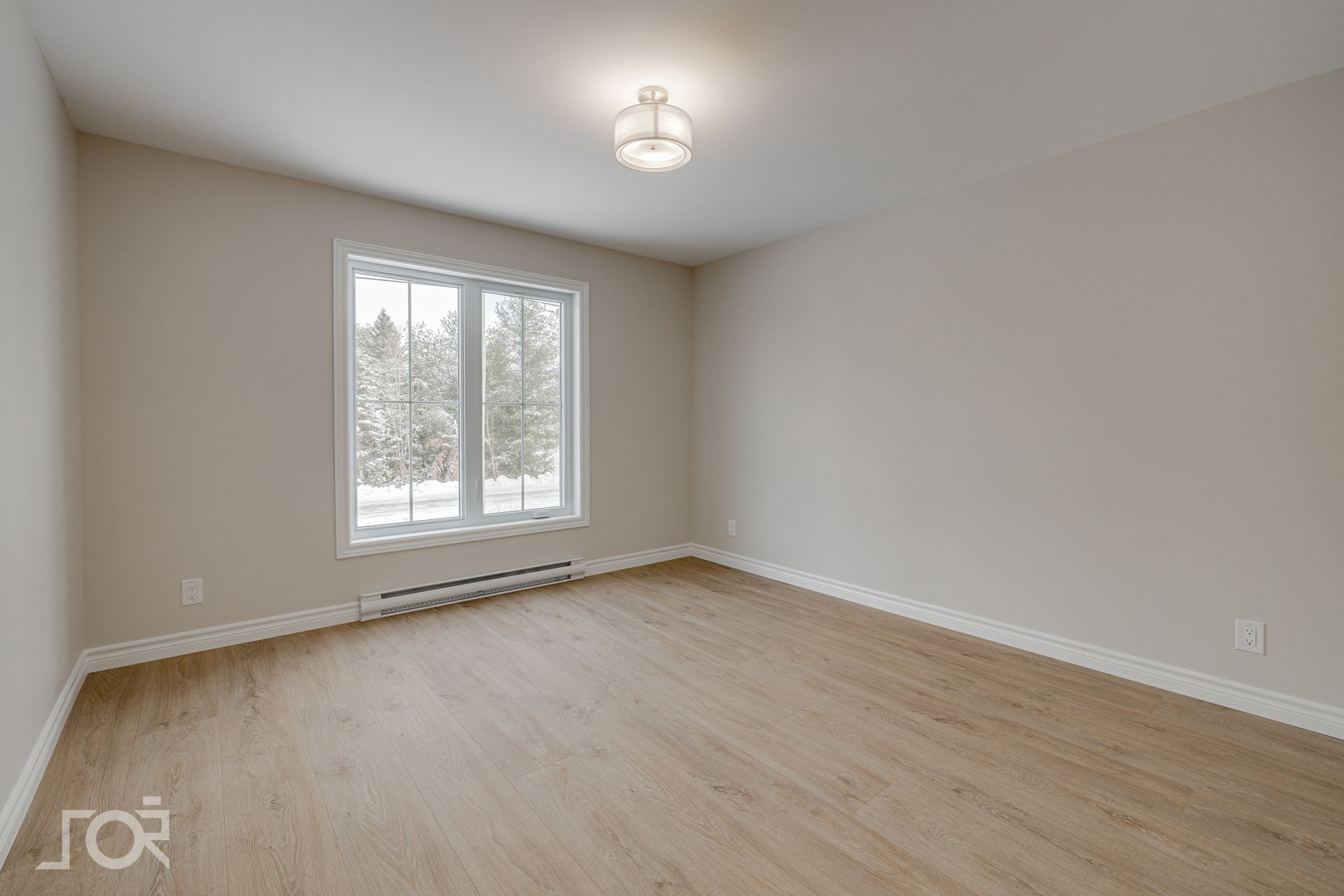 Pièce vide avec parquet clair, une fenêtre et un plafonnier. Murs beiges.