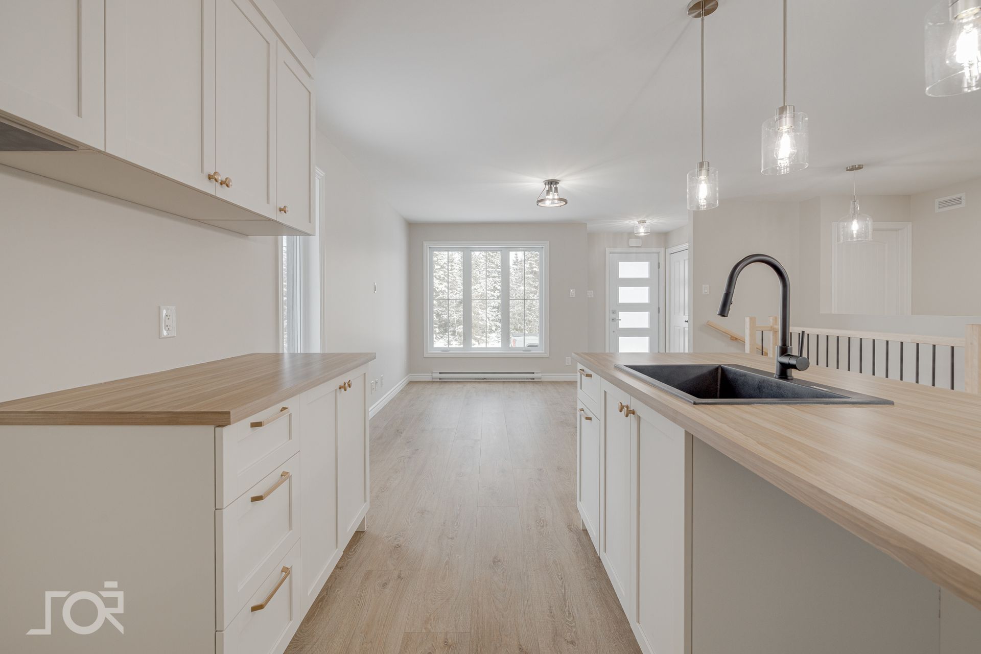 Cuisine moderne et lumineuse avec placards blancs, plans de travail en bois et évier noir.