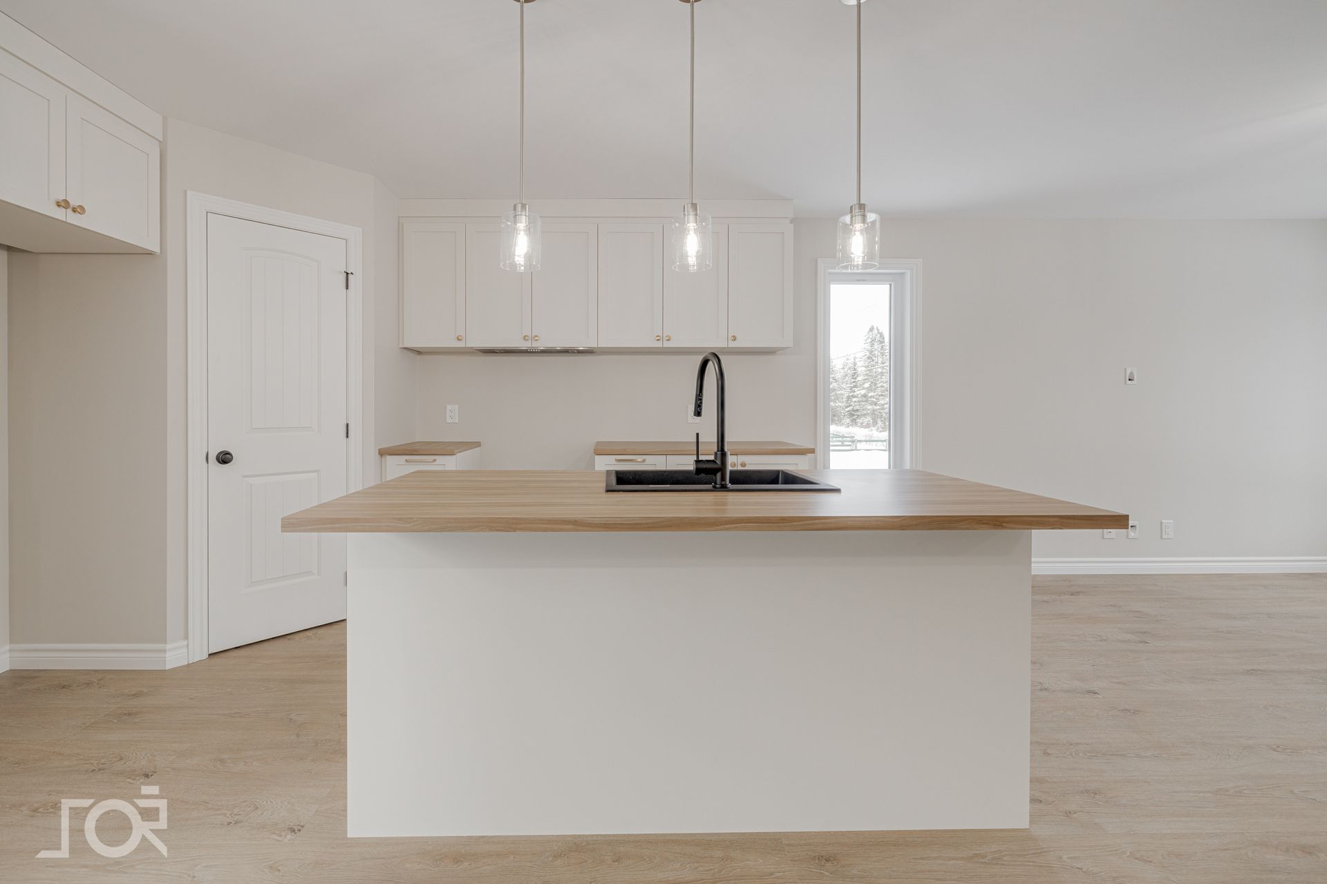 Cuisine moderne avec armoires blanches, îlot avec comptoir en bois, robinet noir, suspensions lumineuses.