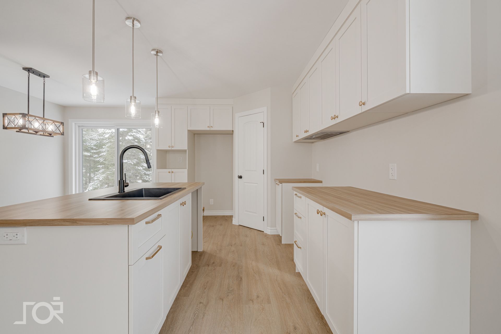 Cuisine moderne blanche avec comptoirs en bois, robinet noir et luminaires suspendus.
