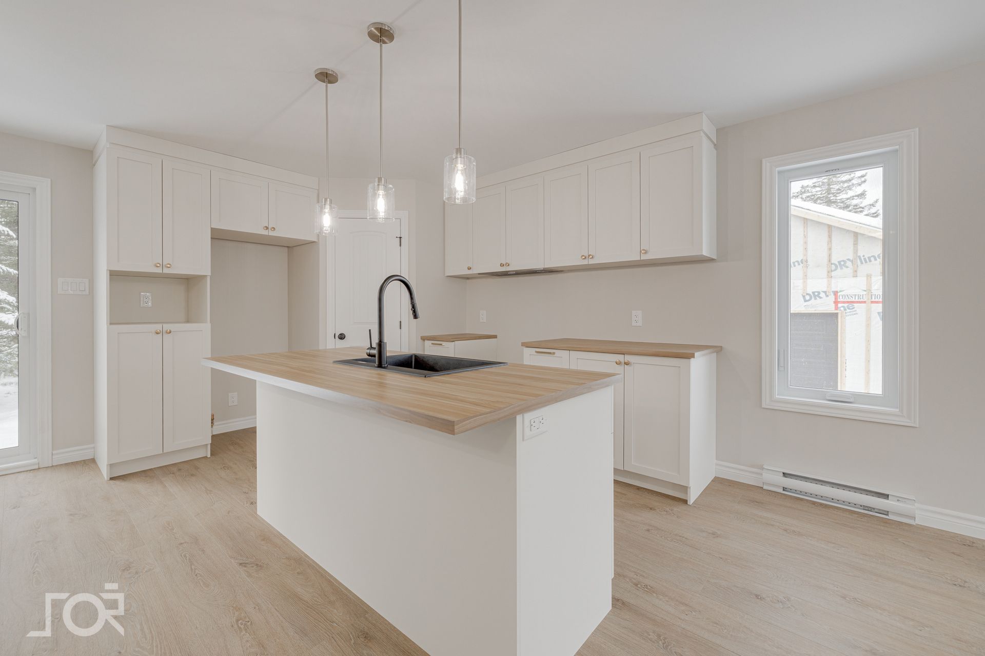 Cuisine moderne avec armoires blanches, comptoirs en bois clair, îlot et parquet.