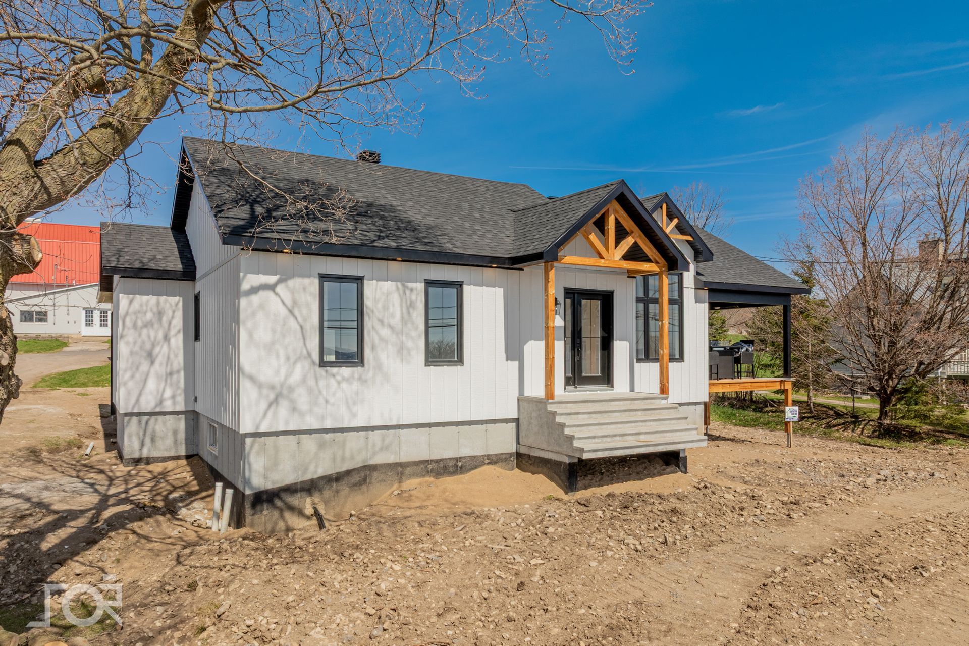 Petite maison blanche en construction, avec toit noir et porche en bois.