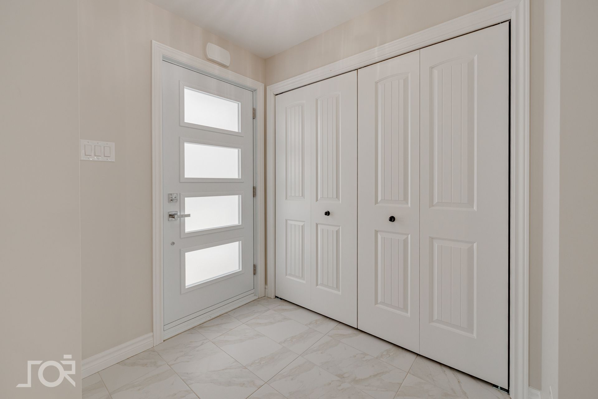 Entrée blanche avec porte d'entrée et portes de placard pliantes ; carrelage gris au sol.