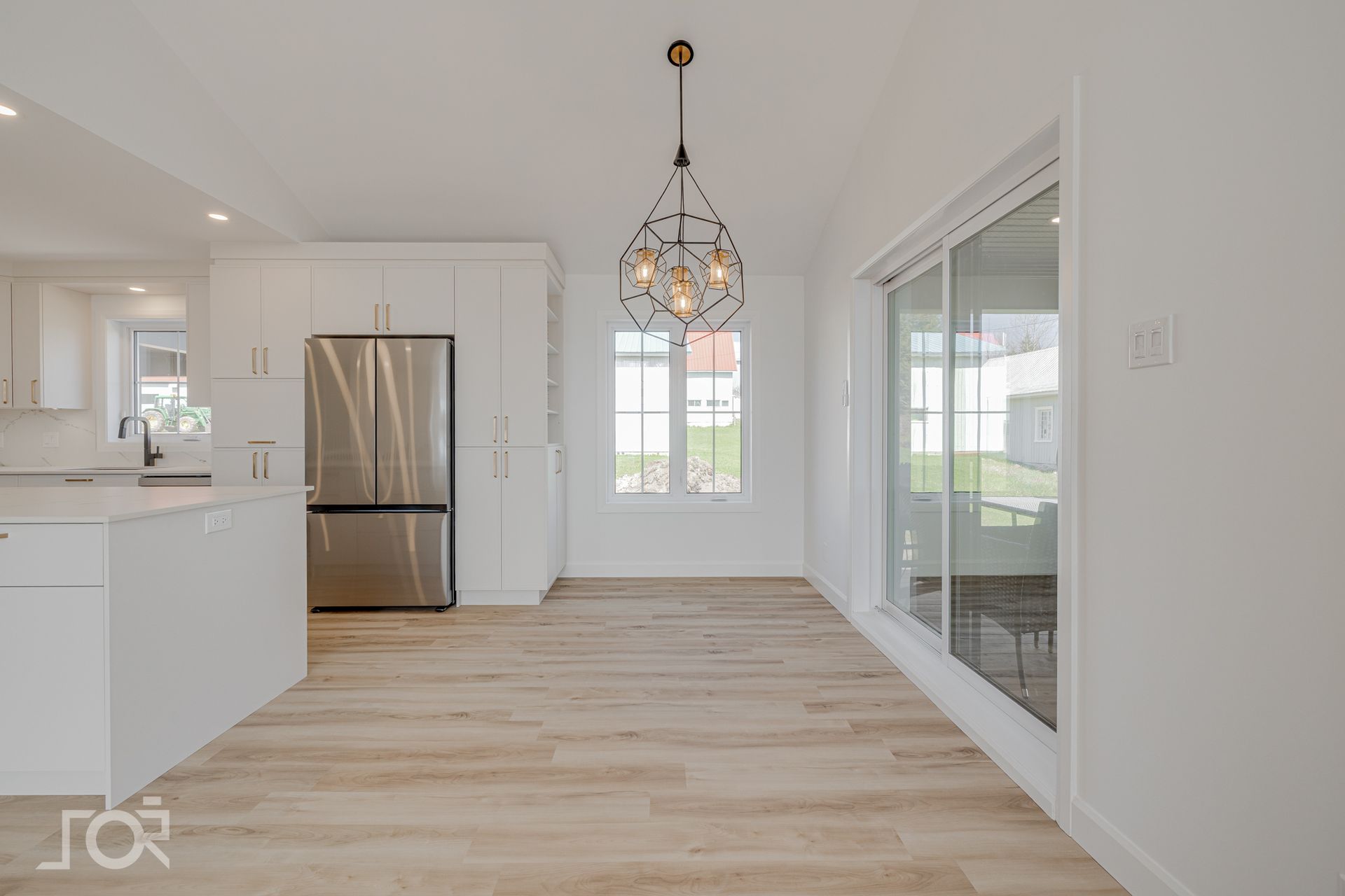Salle à manger lumineuse et moderne avec parquet clair, placards blancs, réfrigérateur en acier inoxydable et luminaire globe.