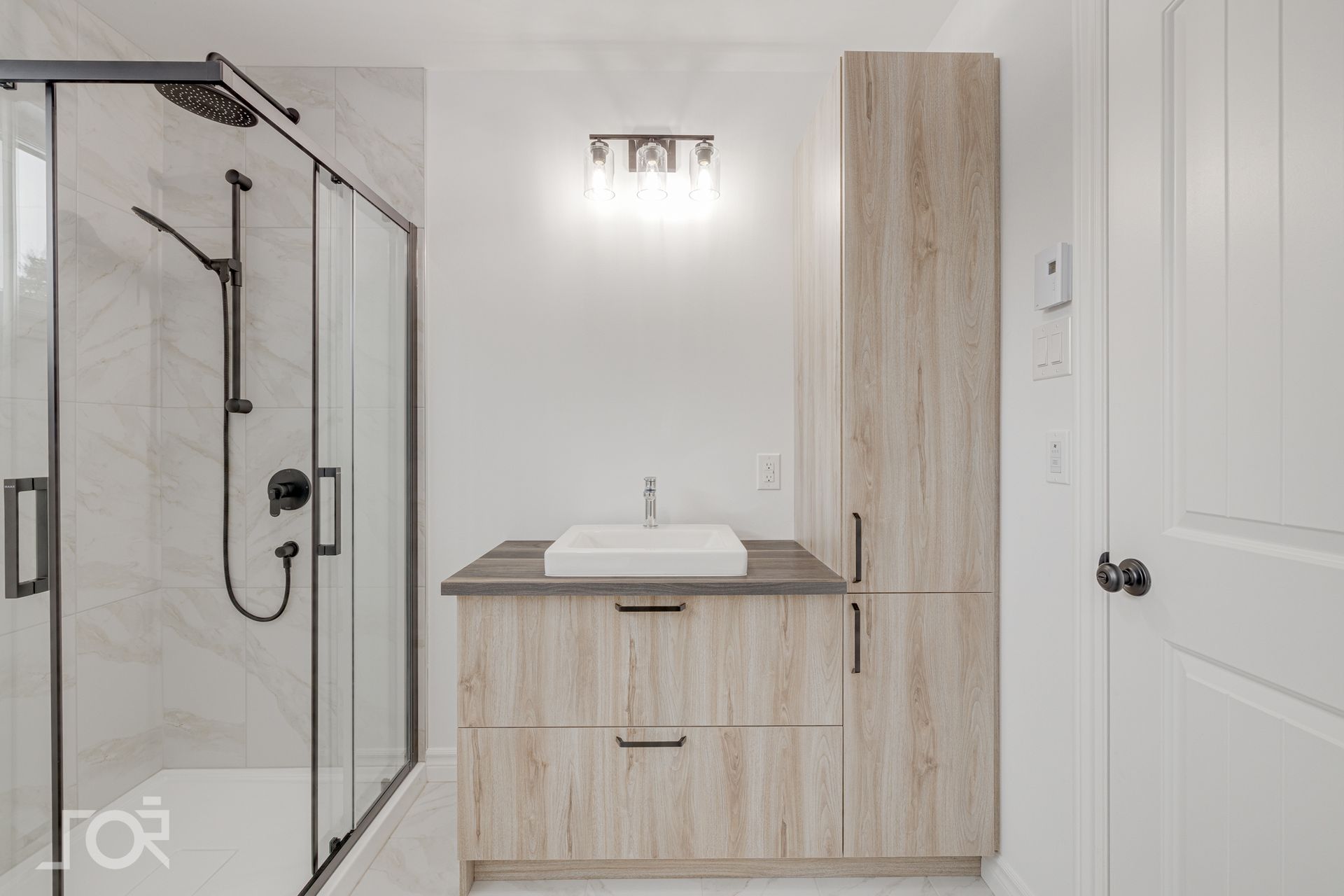 Salle de bains moderne avec douche, meuble-lavabo et armoire haute dans des tons neutres.