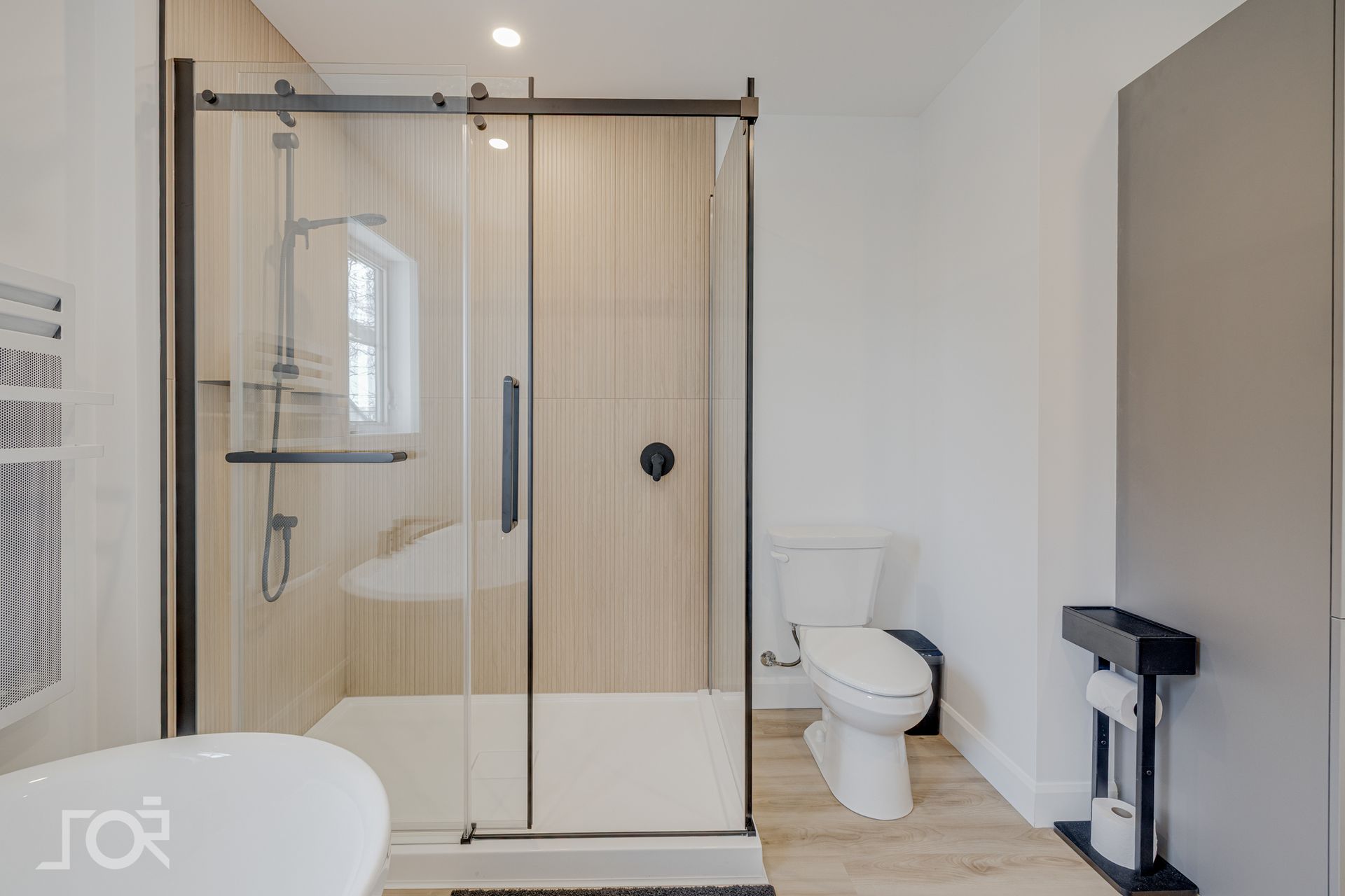 Salle de bains moderne avec douche en verre, toilettes et sol en bois clair.