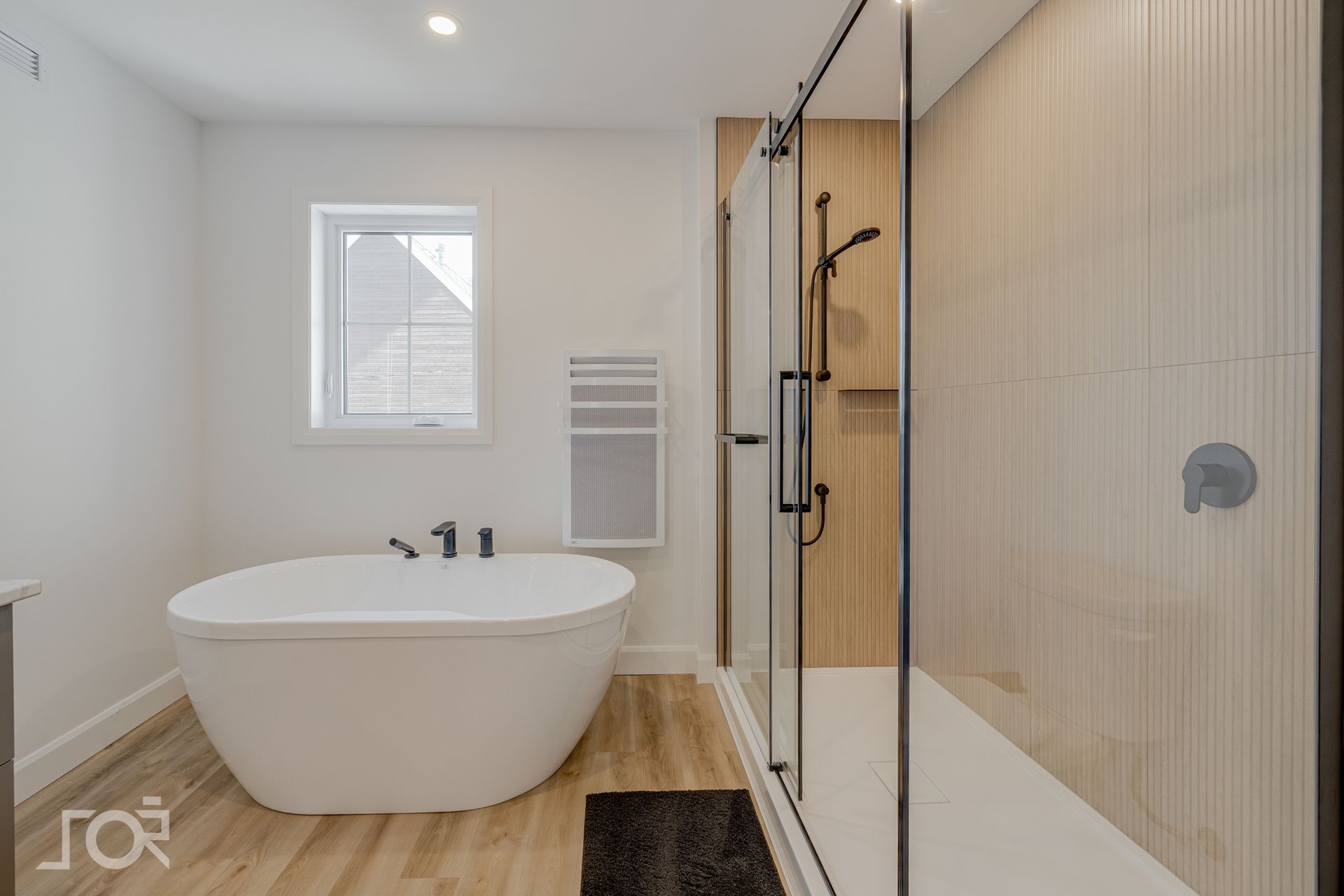 Salle de bains moderne avec baignoire ovale blanche, douche en verre et parquet clair.