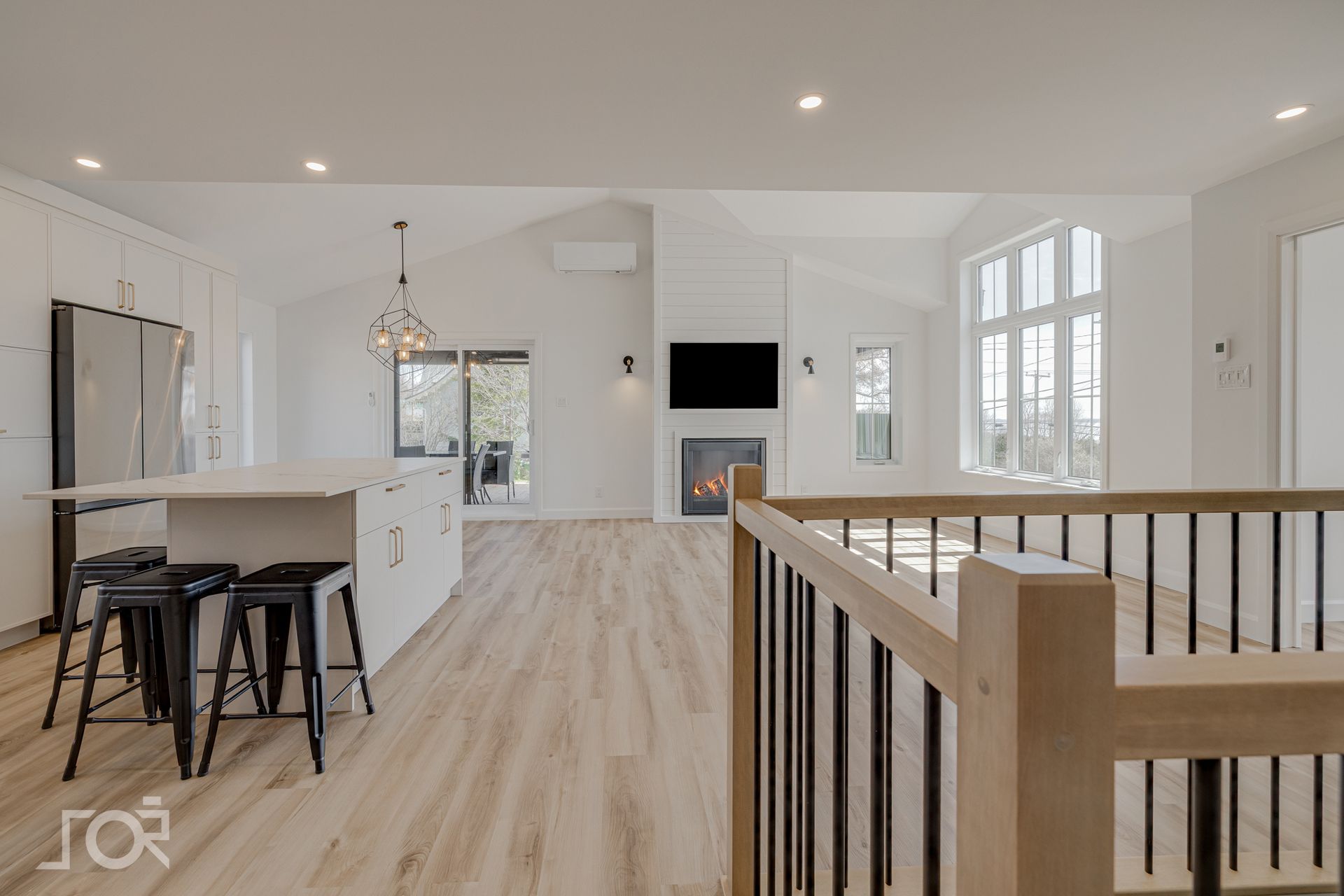 Espace de vie moderne à aire ouverte avec îlot de cuisine, cheminée et grandes fenêtres.