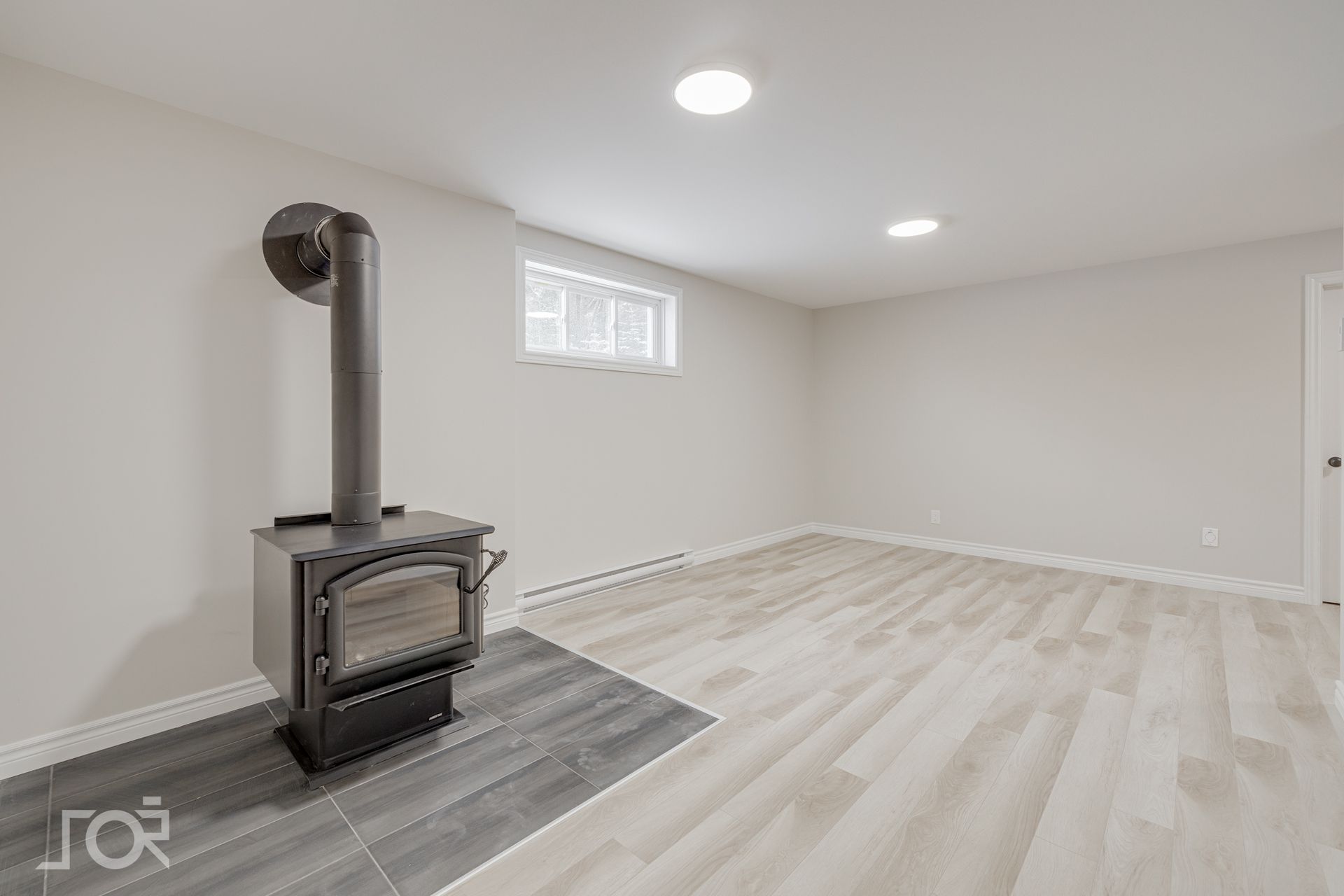 Pièce vide avec un poêle à bois sur un sol carrelé gris.